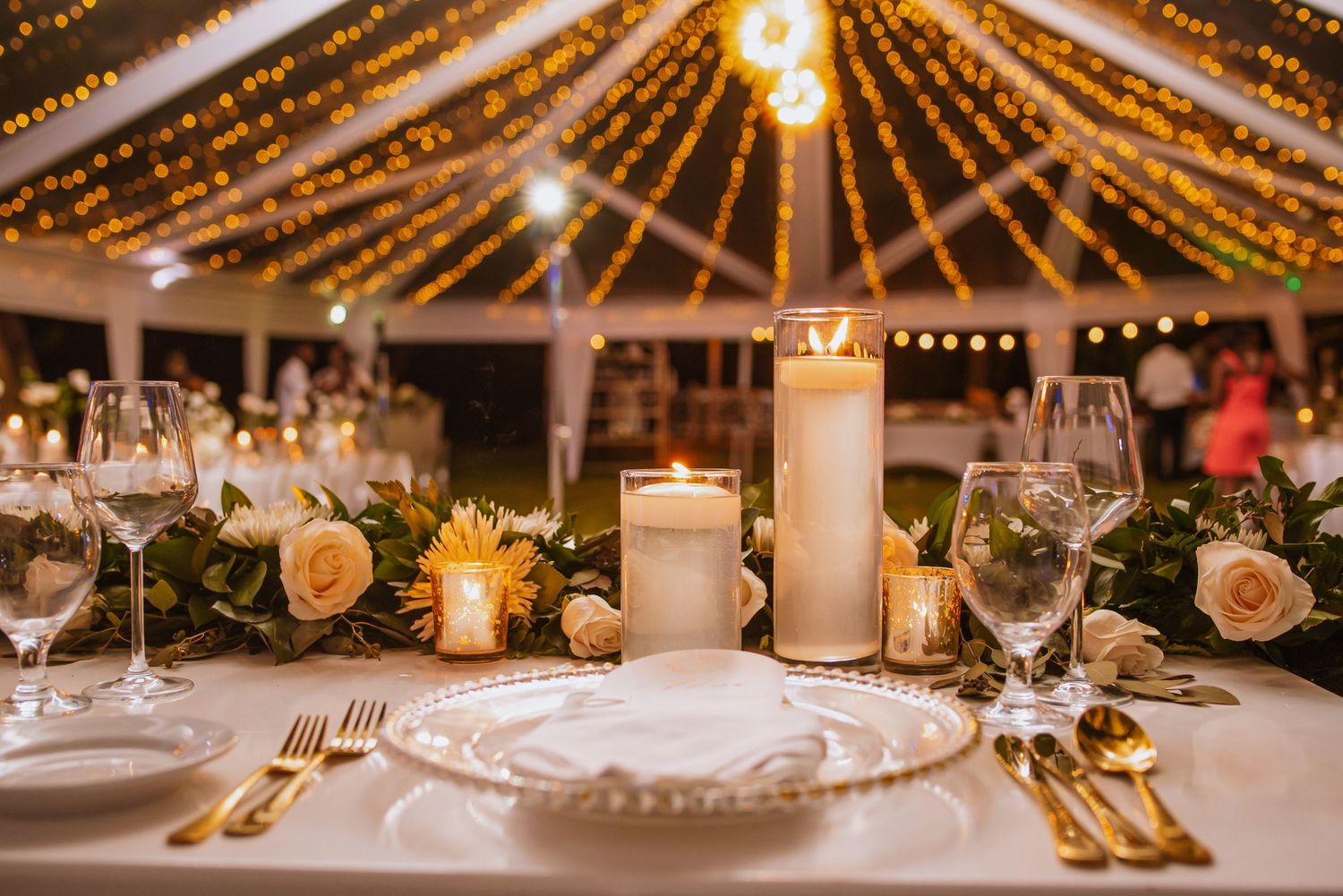 Wedding reception table with string lights overhead, white candles and elegant place settings.