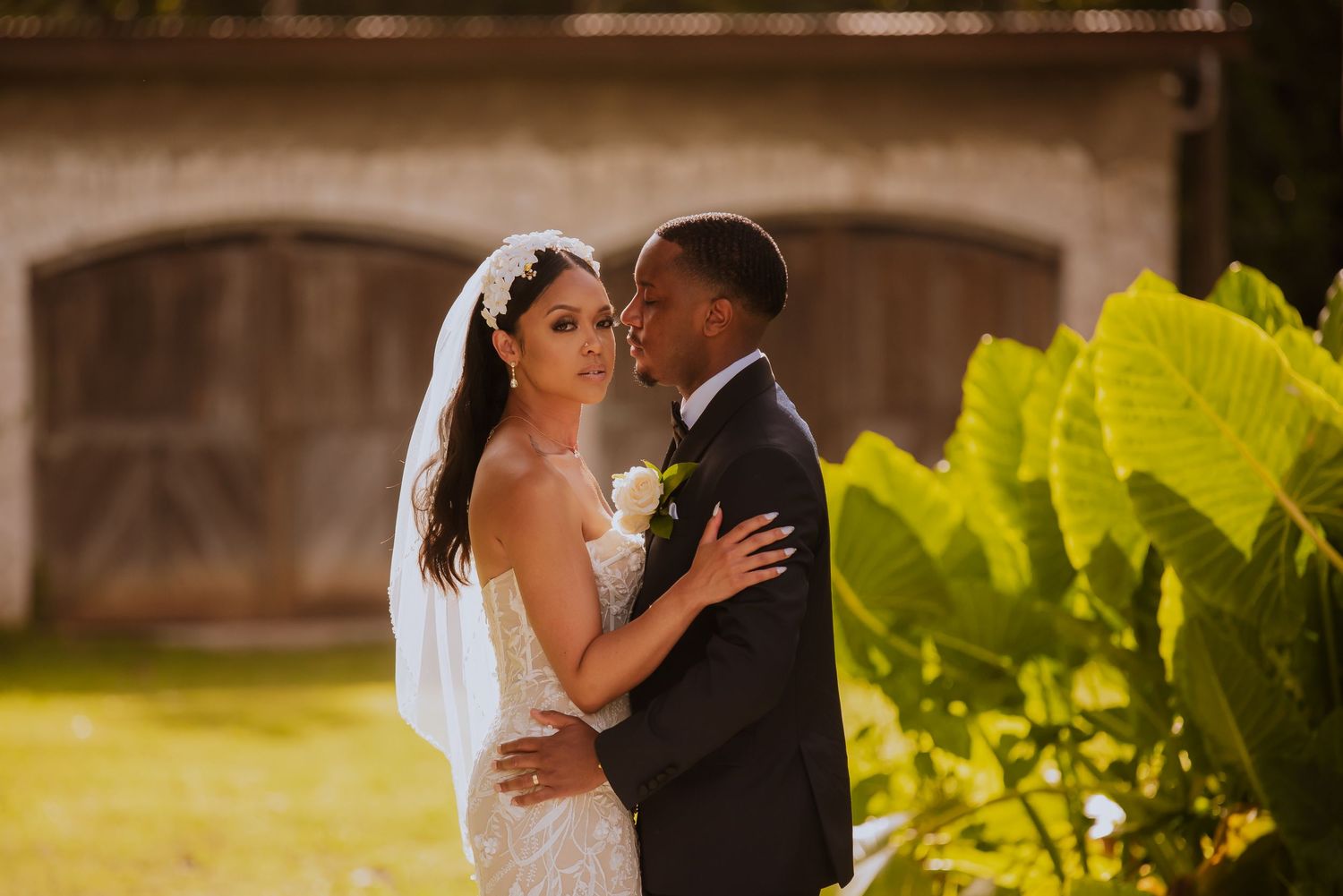 Romantic wedding couple embraces in a garden setting with warm afternoon light.