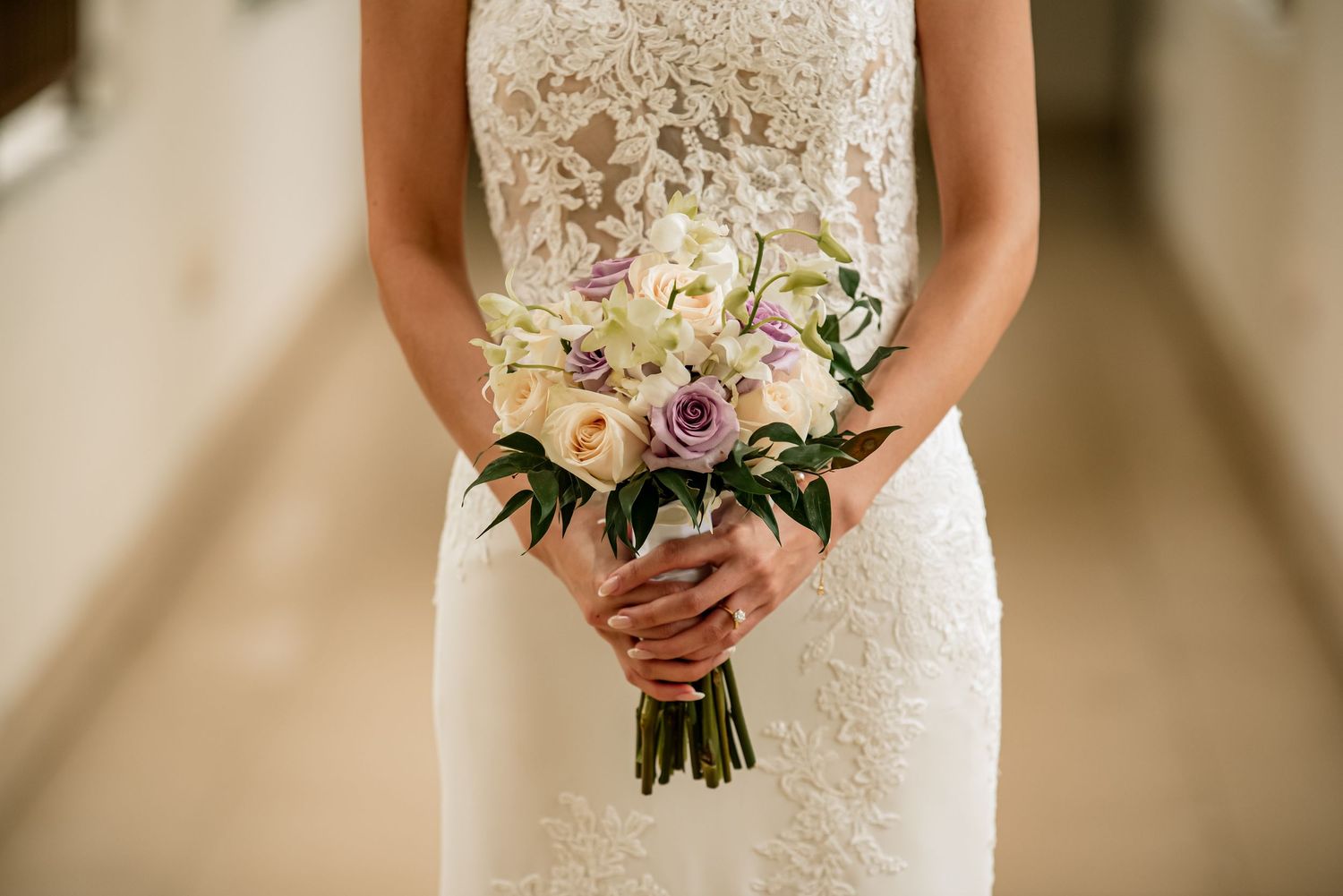 Close-up details of a bride holding a pink and white floral bouquet with her lace wedding dress.