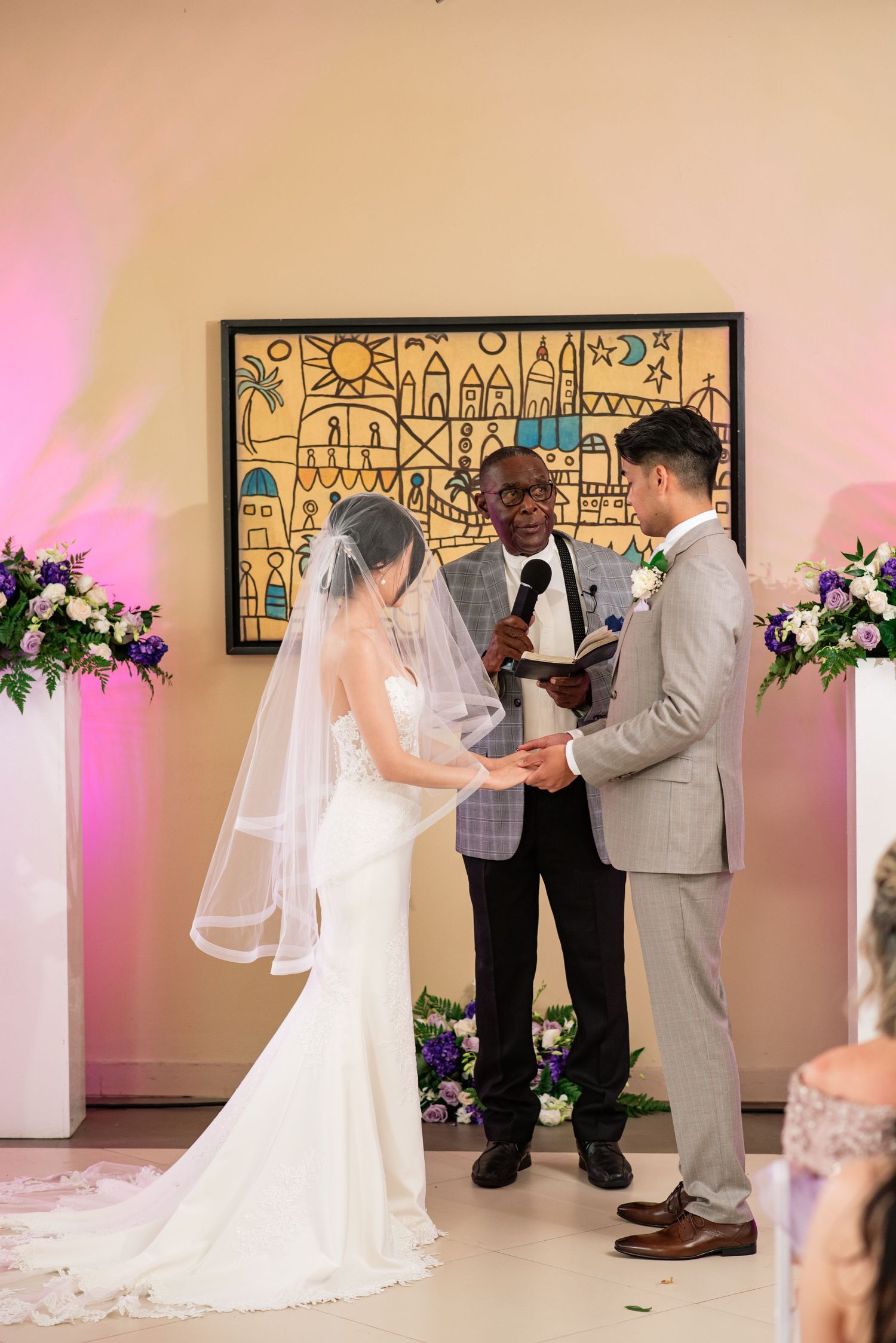 Wedding ceremony taking place in an elegant room with pink lighting and artistic decor.