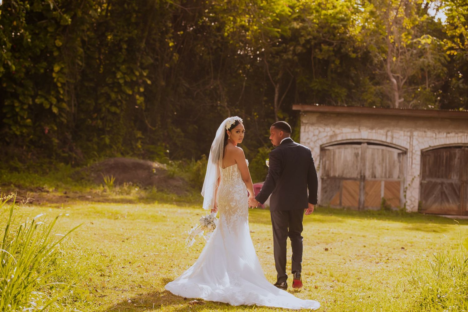 A wedding couple captured in silhouette against a sunlit garden backdrop.