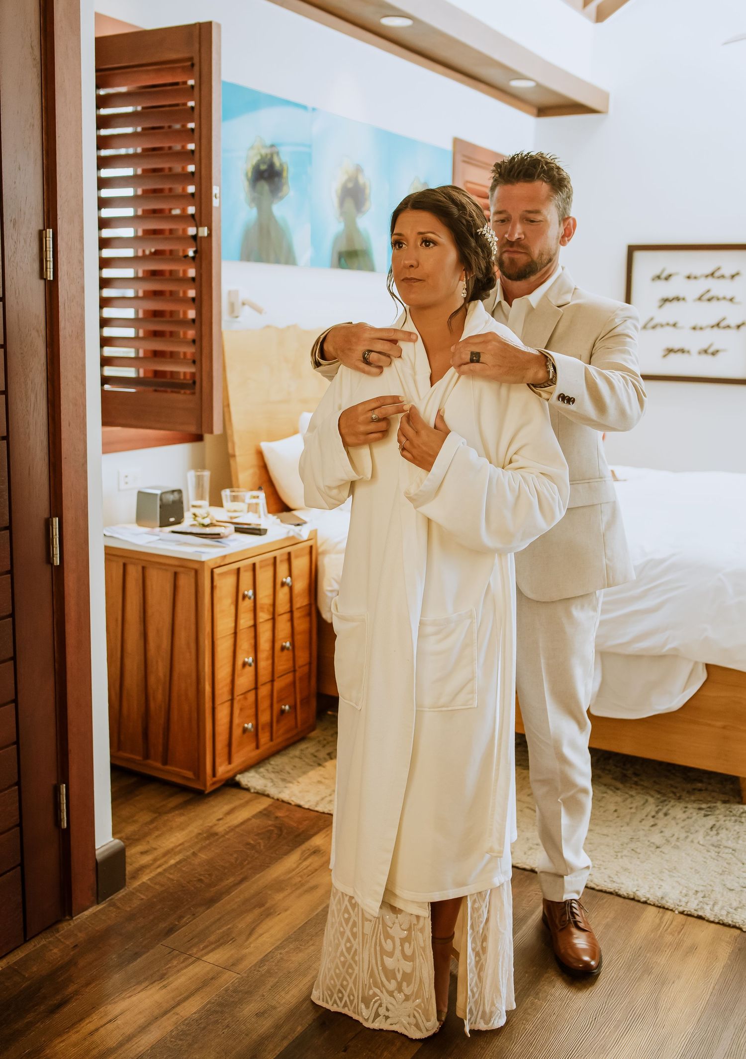 Wedding preparation scene in a bright room with wooden furniture and white robes.
