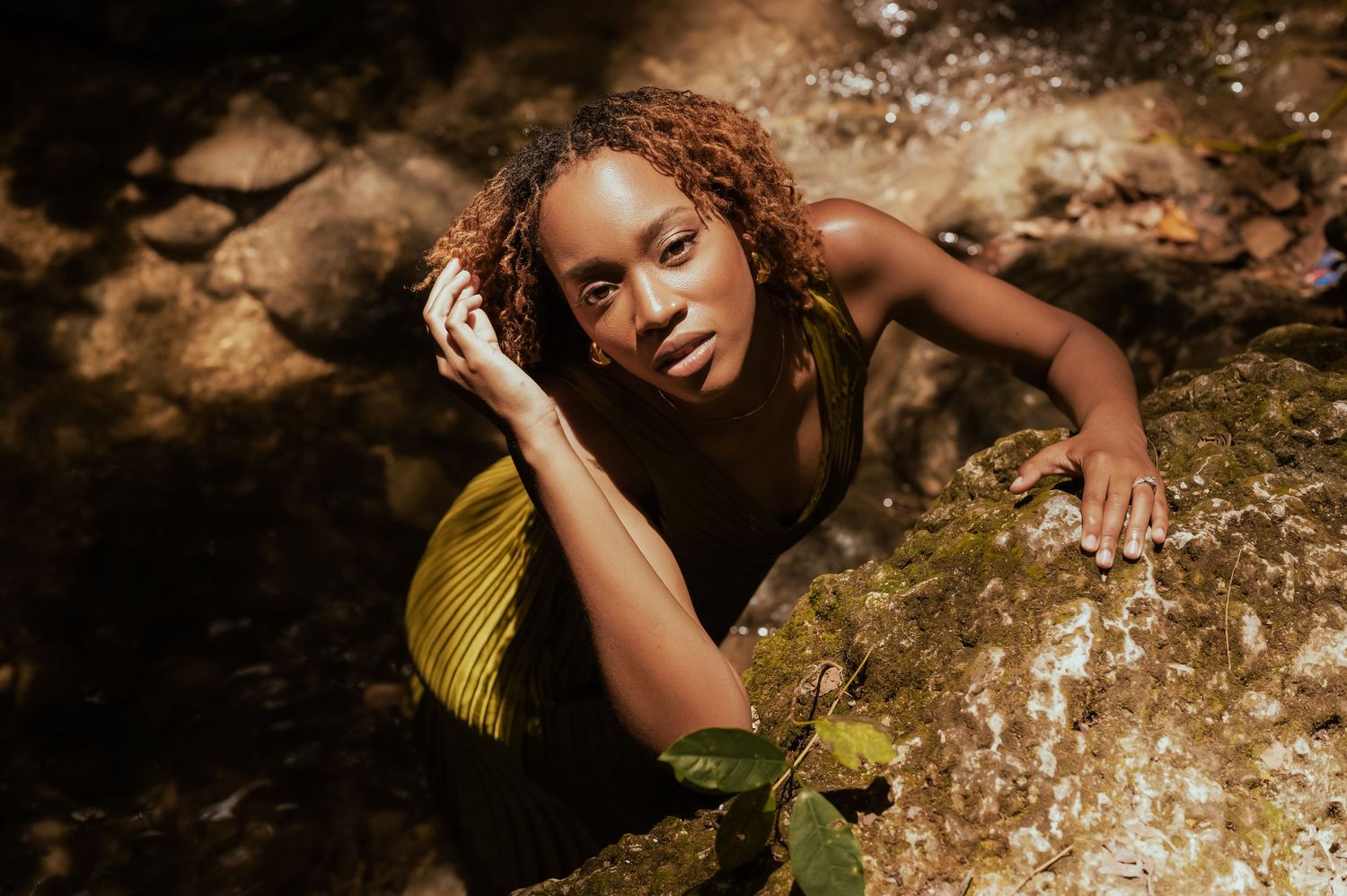 Woman in yellow dress poses artistically near a cascading waterfall.