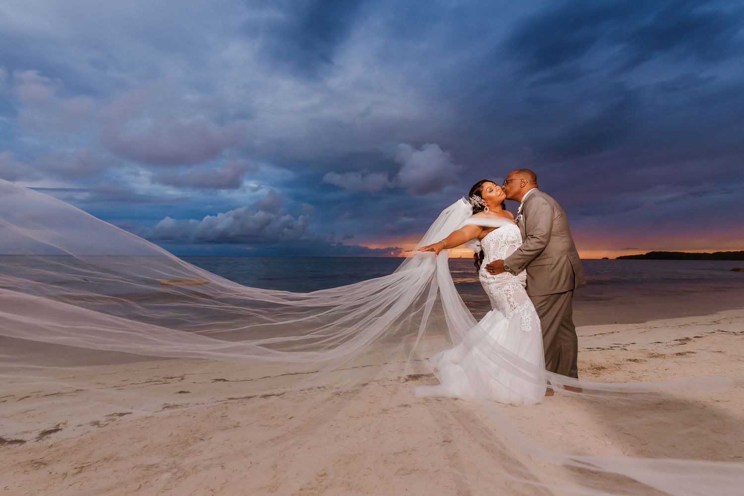 Dramatic desert wedding photos with flowing veil against sunset sky.