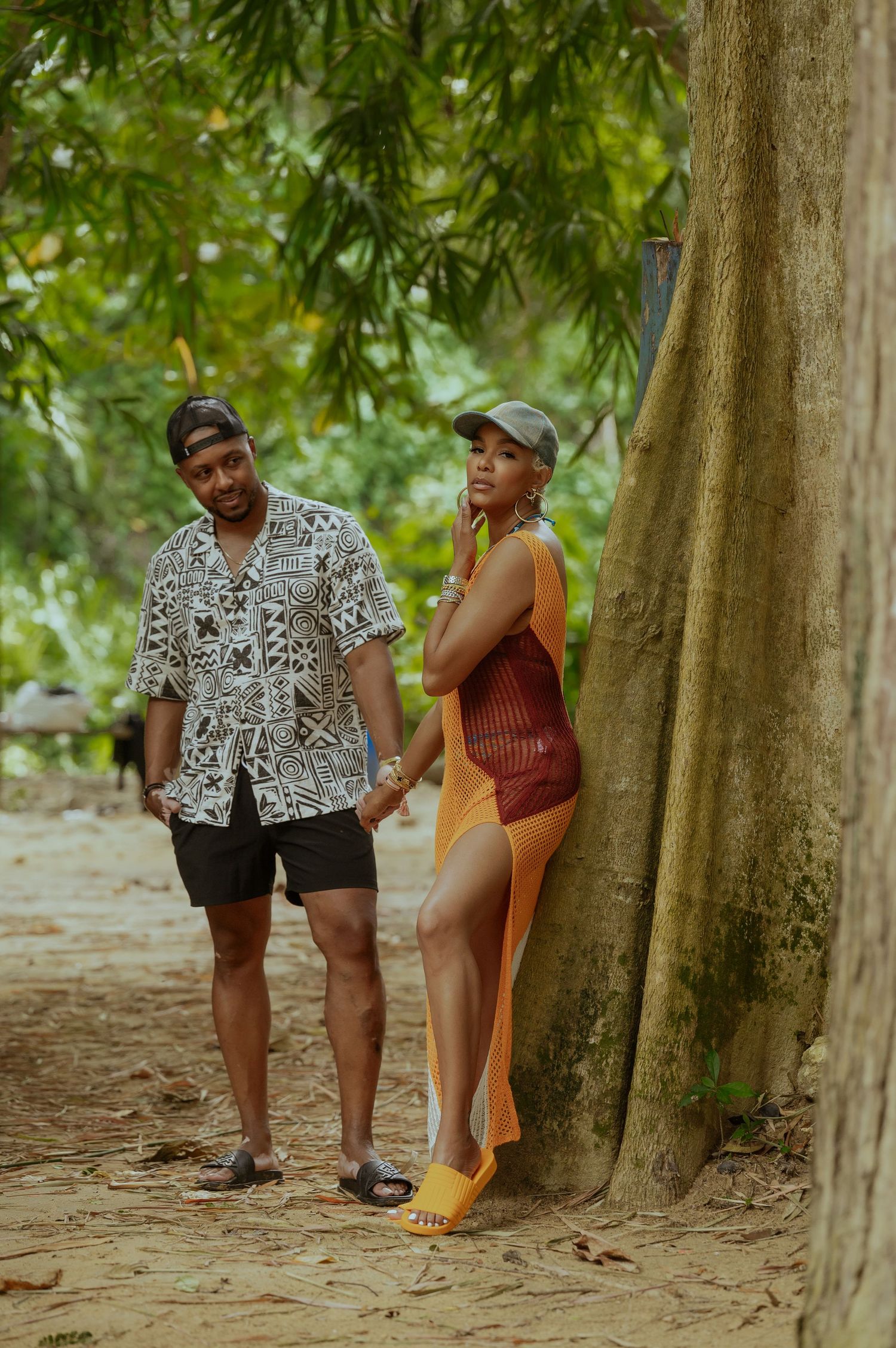 Couple takes playful engagement photos in a wooded area with natural lighting and trees.