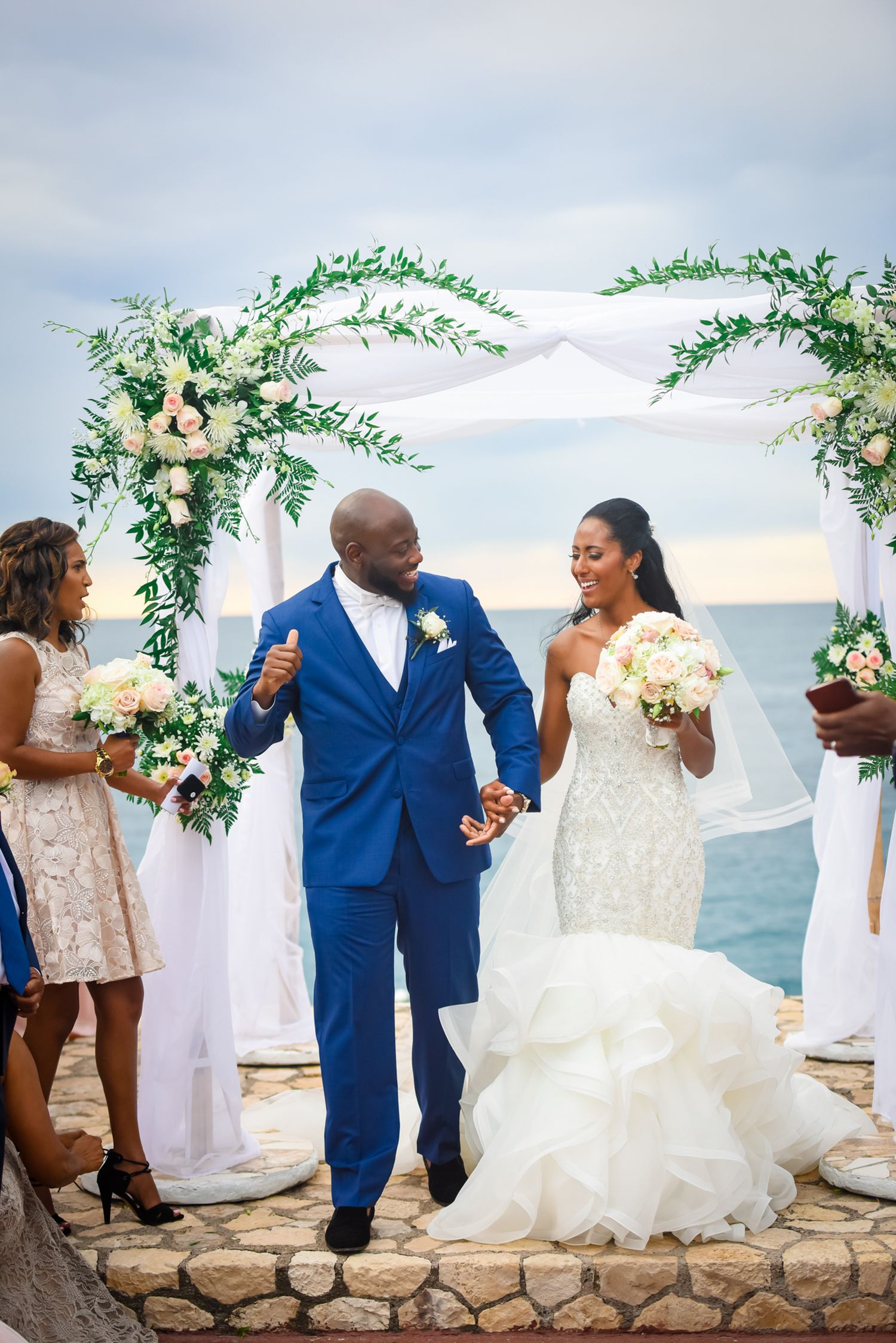 Newlyweds celebrate under a floral arch during their oceanside wedding ceremony.