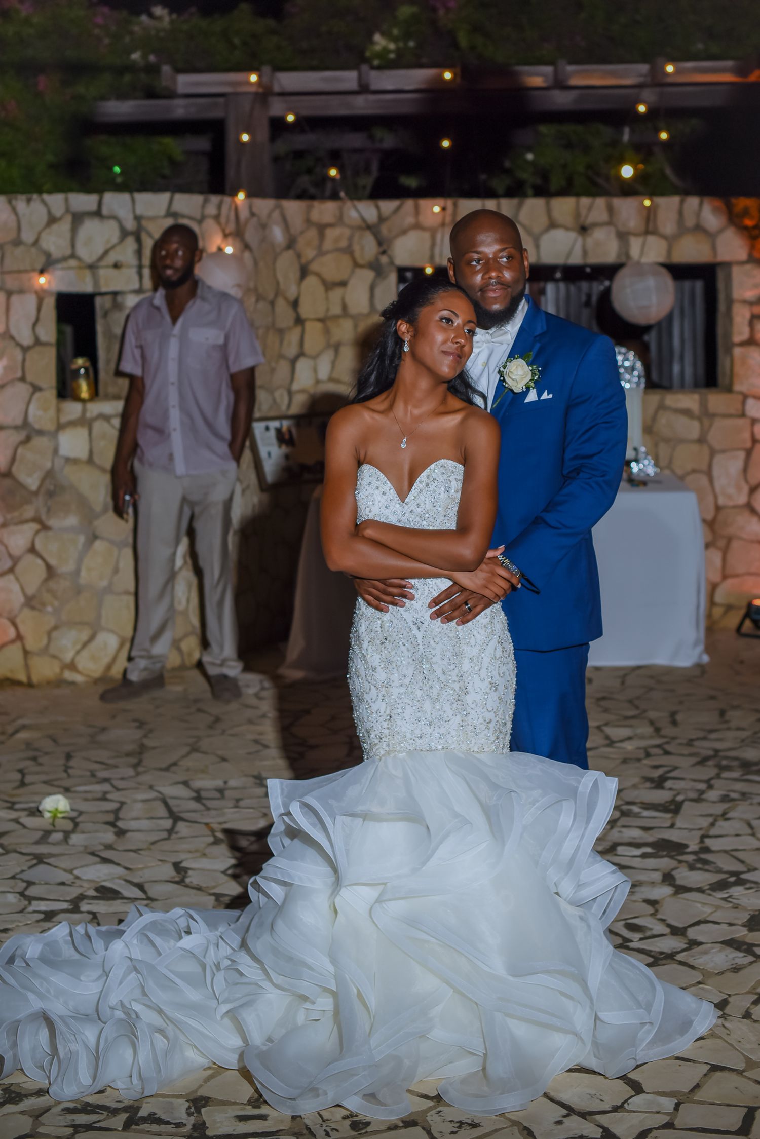 Newlyweds sharing an intimate dance moment on stone patio with decorative lighting.