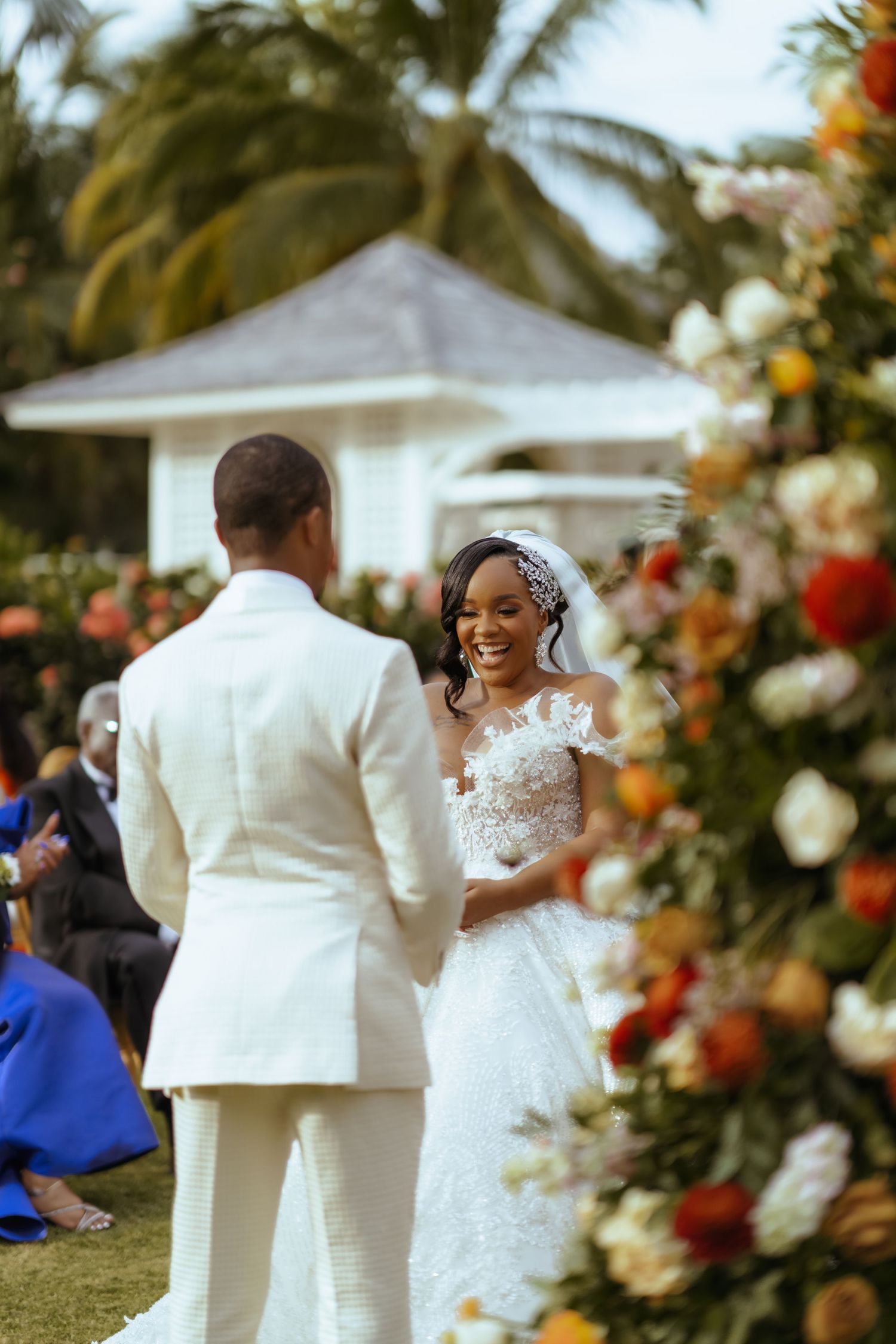 Outdoor wedding ceremony with floral arrangements and a white gazebo in the background.