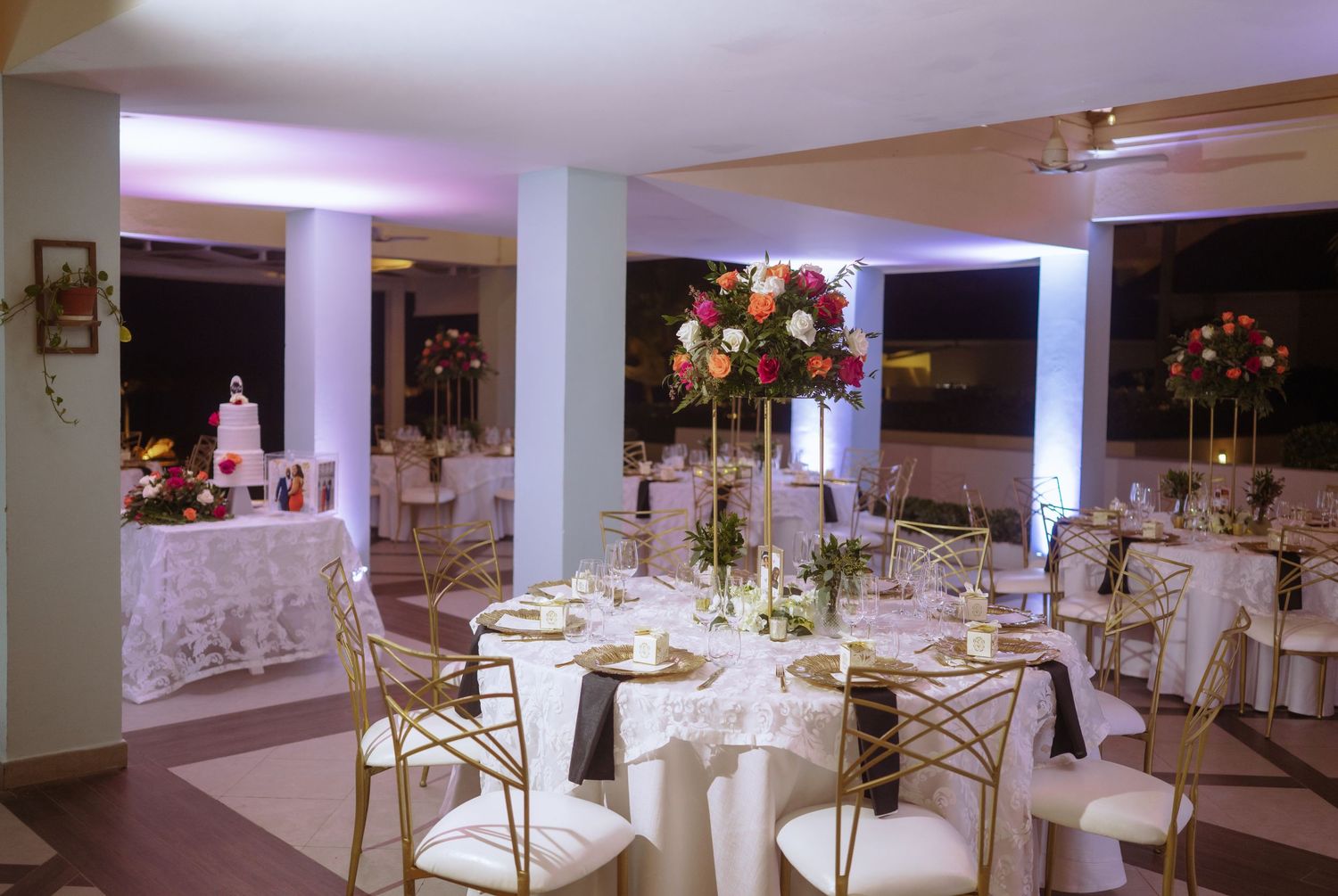 Modern wedding reception venue with white tables and gold chairs set for celebration.