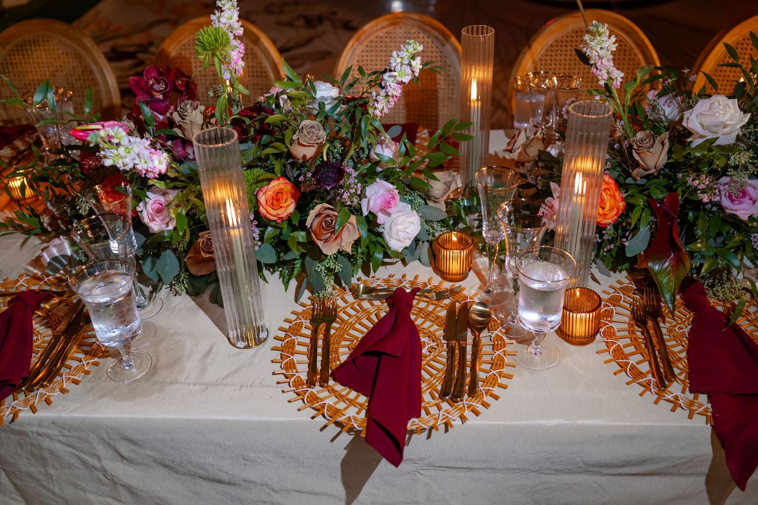 Elegant wedding reception table decorated with burgundy florals, candles and gold accents.