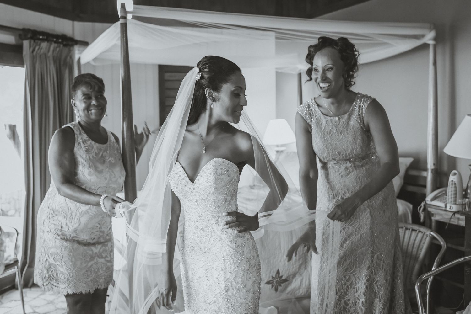 Bridesmaids in lace dresses assist with wedding preparations in a bright interior space.