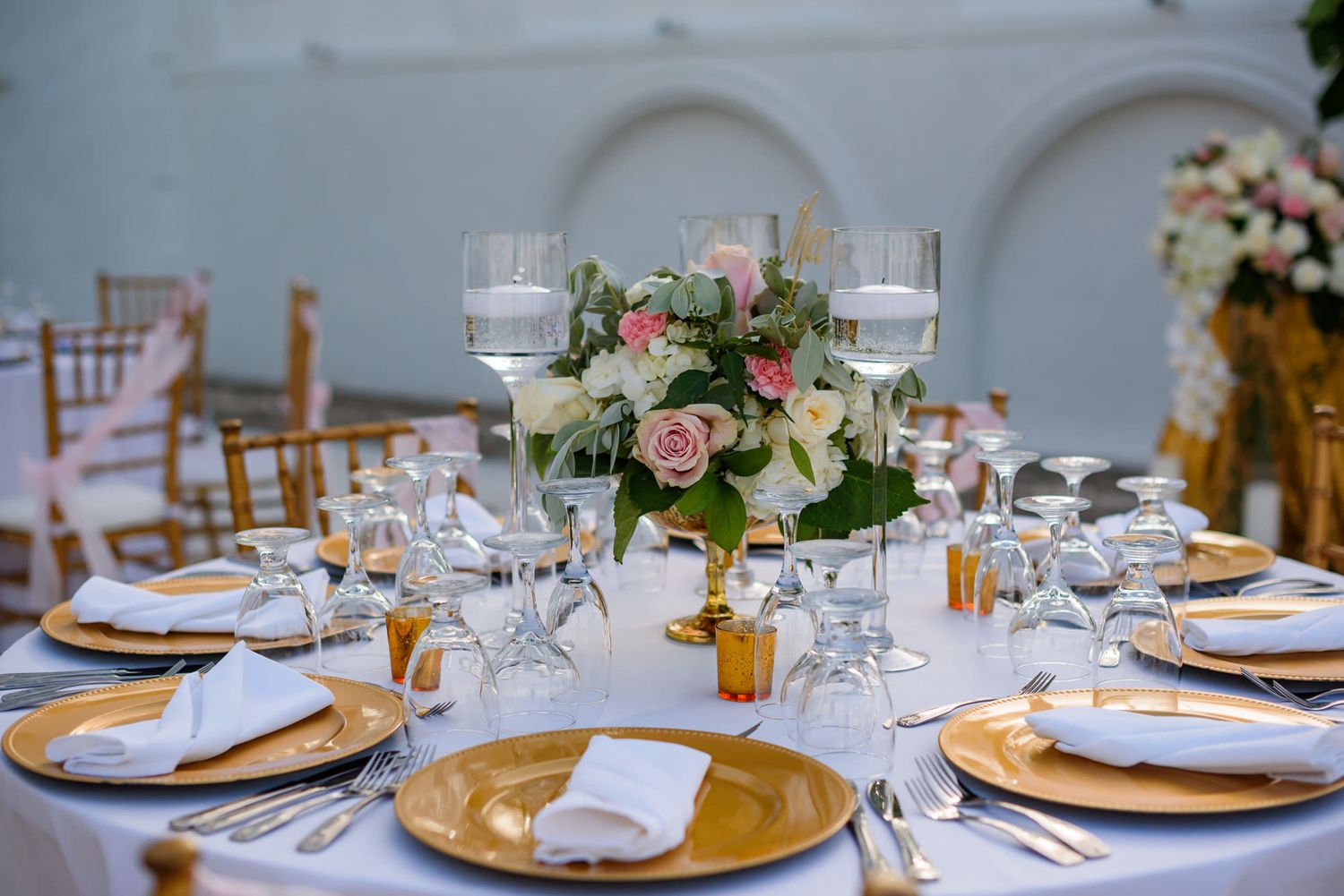 Wedding reception dining tables set with gold chargers, white napkins and floral arrangements.