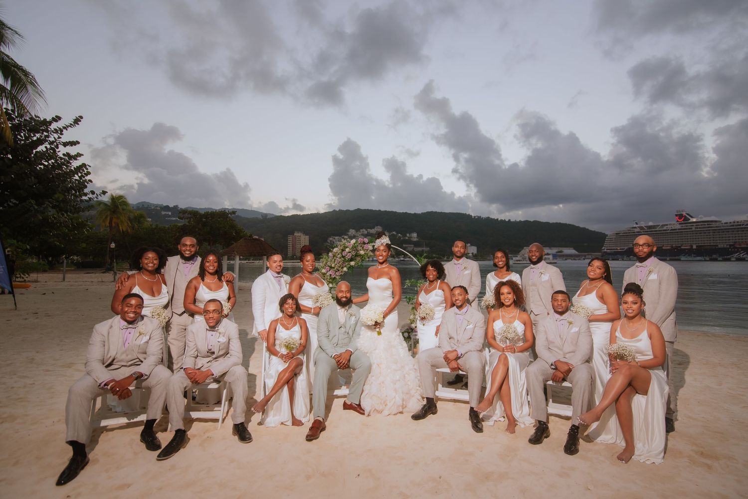 Wedding party poses together on beach at sunset for group photo.