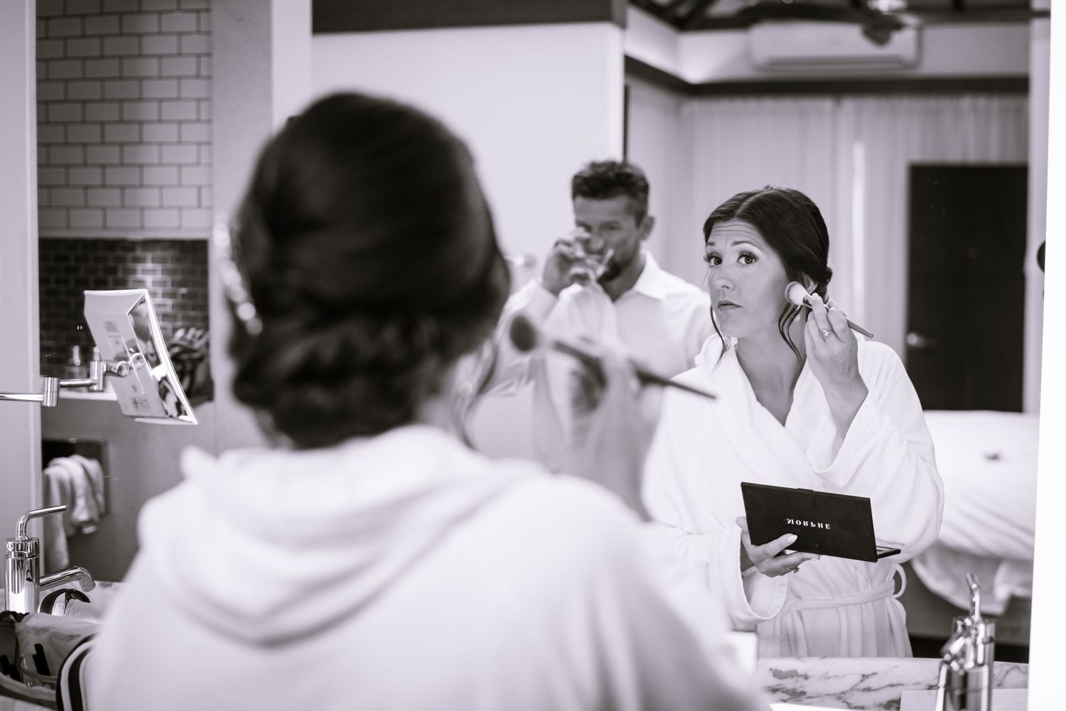 Wedding party getting ready in a bright indoor space wearing white robes and formal attire.
