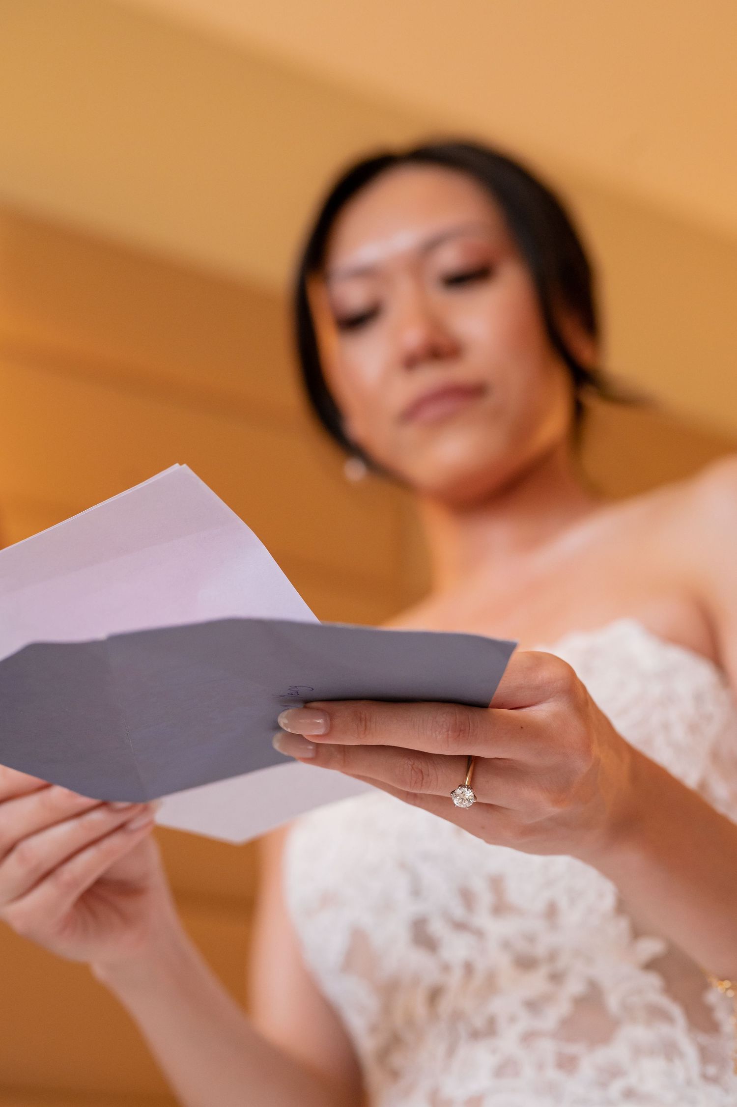 Bride in lace dress reading a letter during wedding preparations.