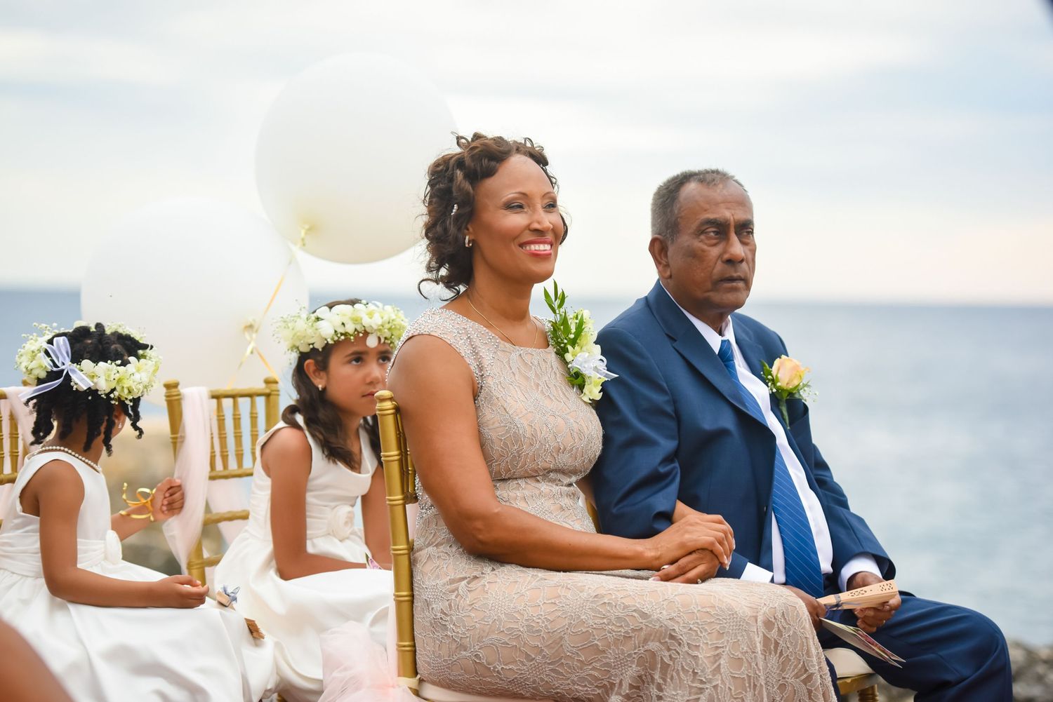 Beachside wedding ceremony with guests seated on gold chairs overlooking the ocean.