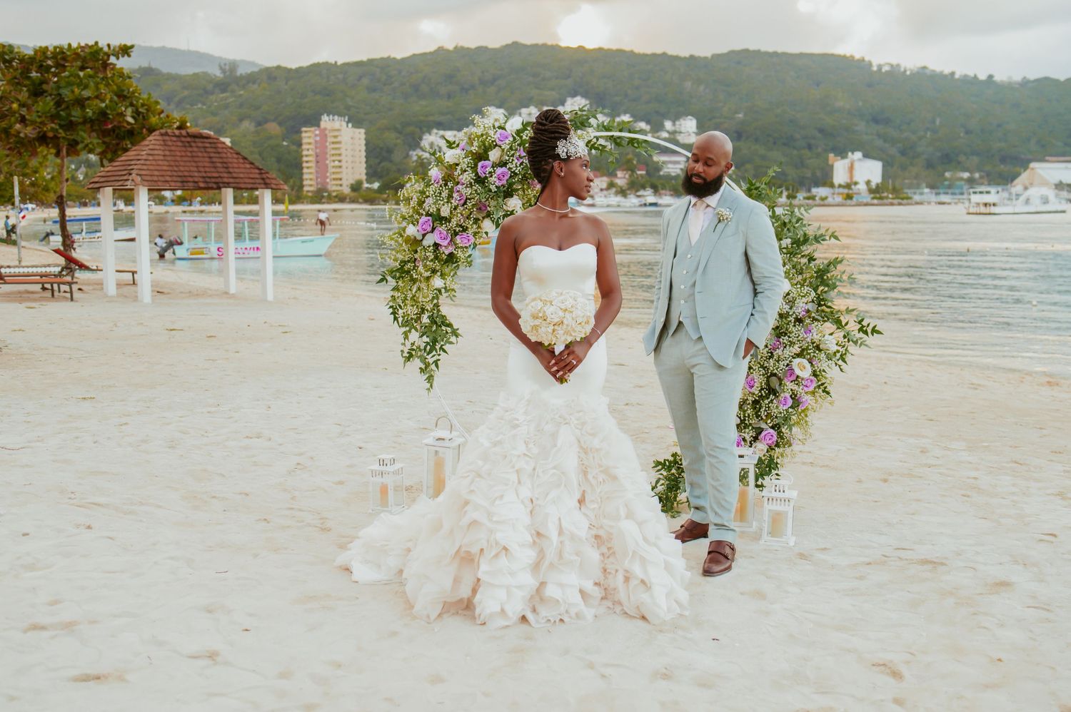 Elegant beach wedding ceremony setup with floral arch and ocean backdrop at sunset.