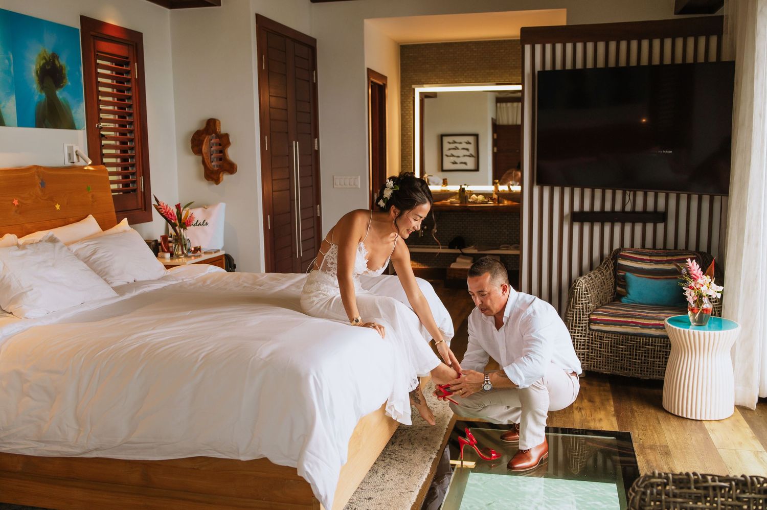 A couple in white outfits share intimate moments on a bed in a tropical resort room.