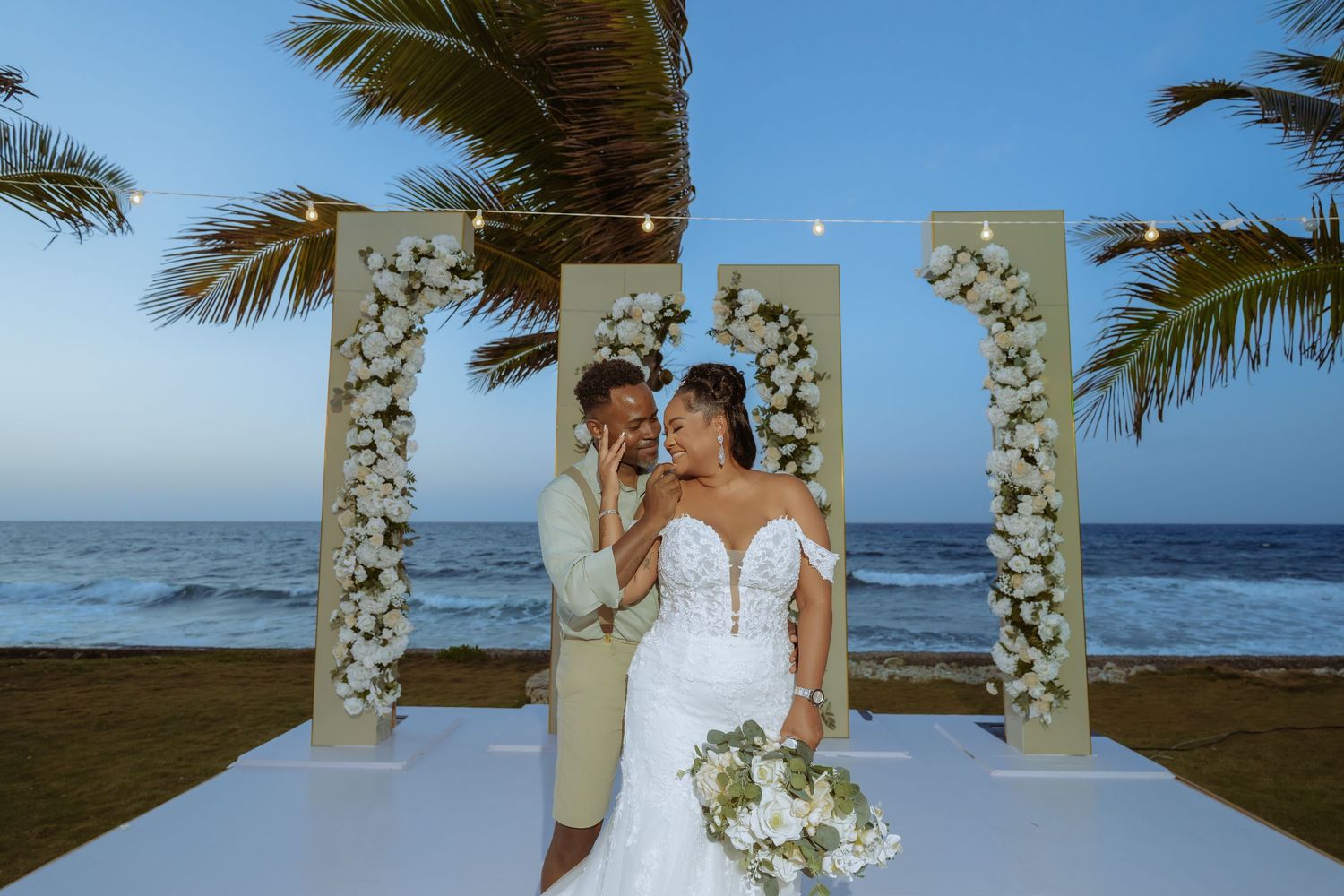 Beachside wedding ceremony setup with white floral arch and ocean backdrop.