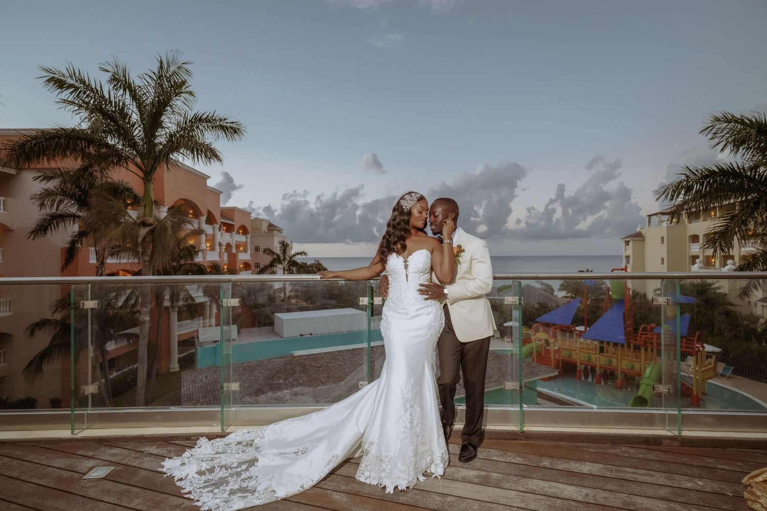 Wedding couple photographed against oceanfront resort backdrop with palm trees.