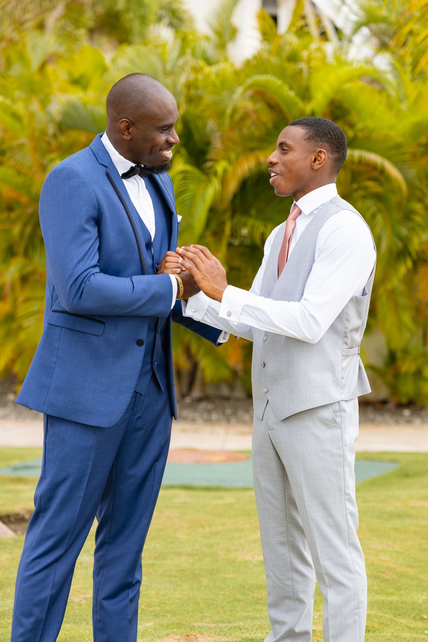 Wedding party members in blue and light suits share playful moments on tropical grounds.
