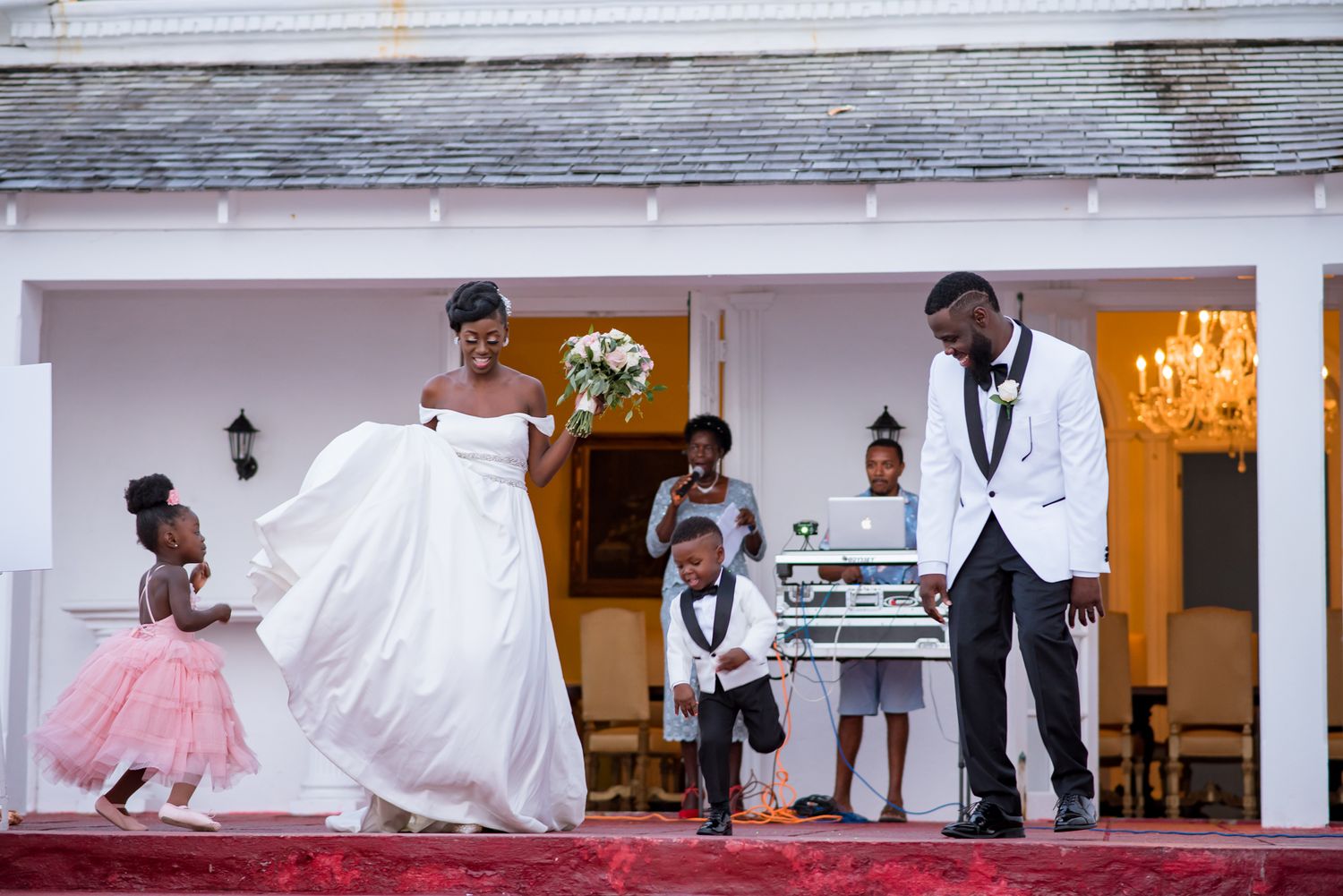 Wedding celebration scene at an elegant white venue with festive lighting.
