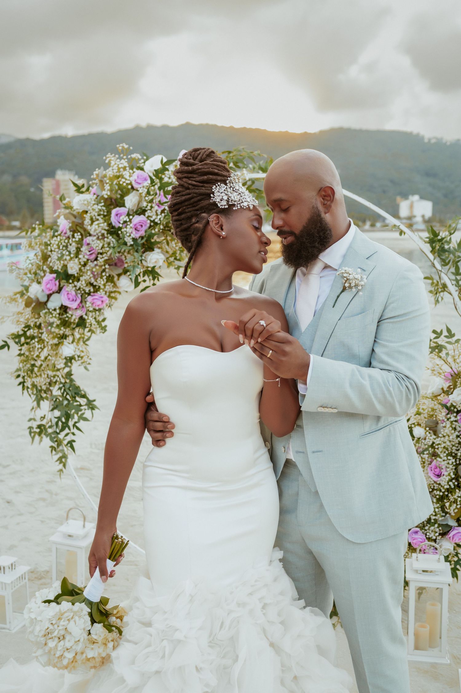 Romantic beach wedding couple shares intimate dance under floral arch with ocean view.
