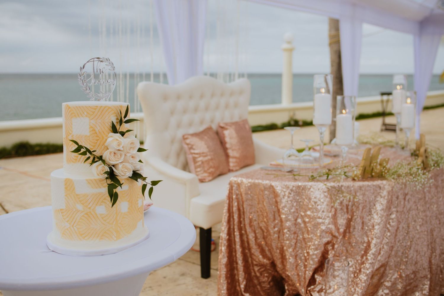 Elegant wedding cake display with floral accents next to a rose gold sequined sweetheart table.