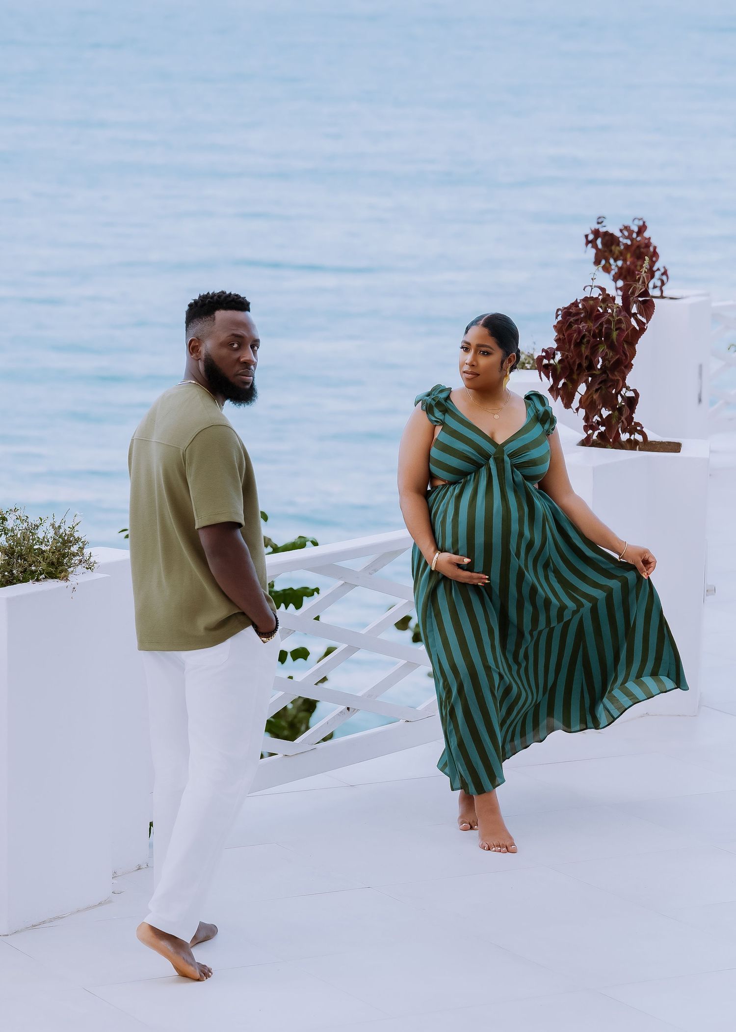 Romantic photoshoot on white Mediterranean steps with striped green dress and coastal backdrop.