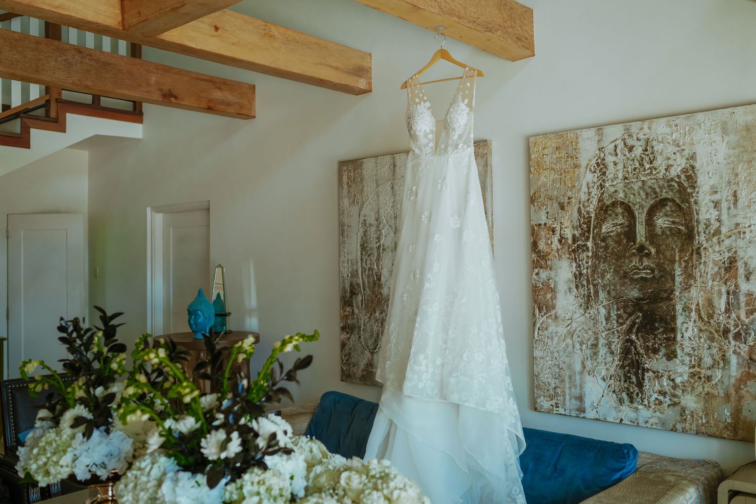 Wedding dress hanging in rustic room with wooden beams and natural light.