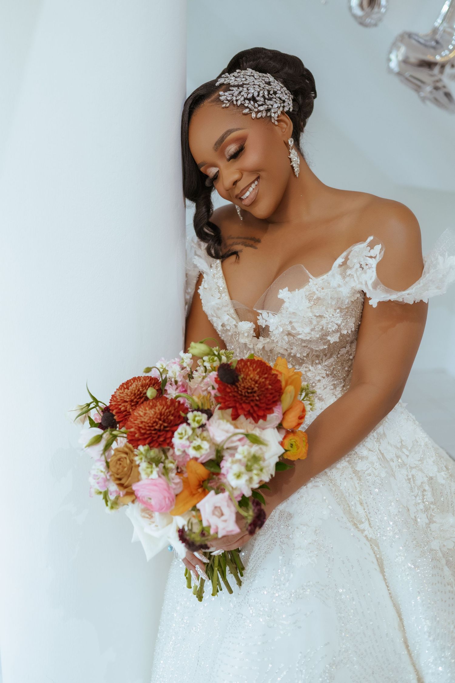 A close-up shot of a bride in an off-shoulder lace gown holding a vibrant autumn-colored bouquet.