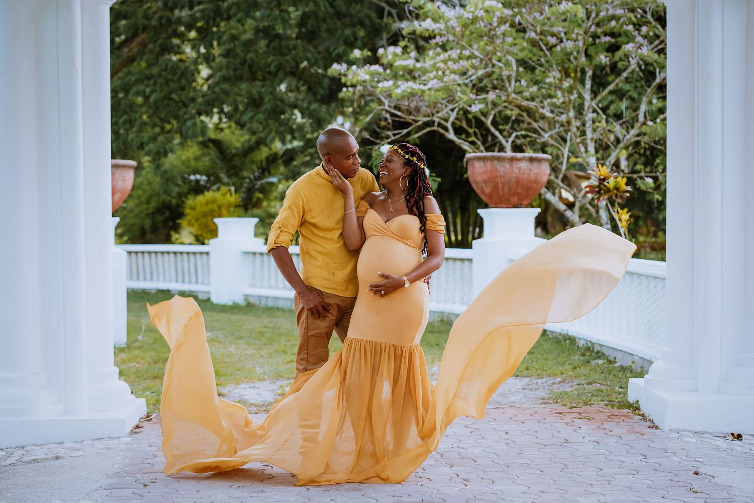 Couple embraces in romantic maternity photo as flowing yellow dress catches the breeze.