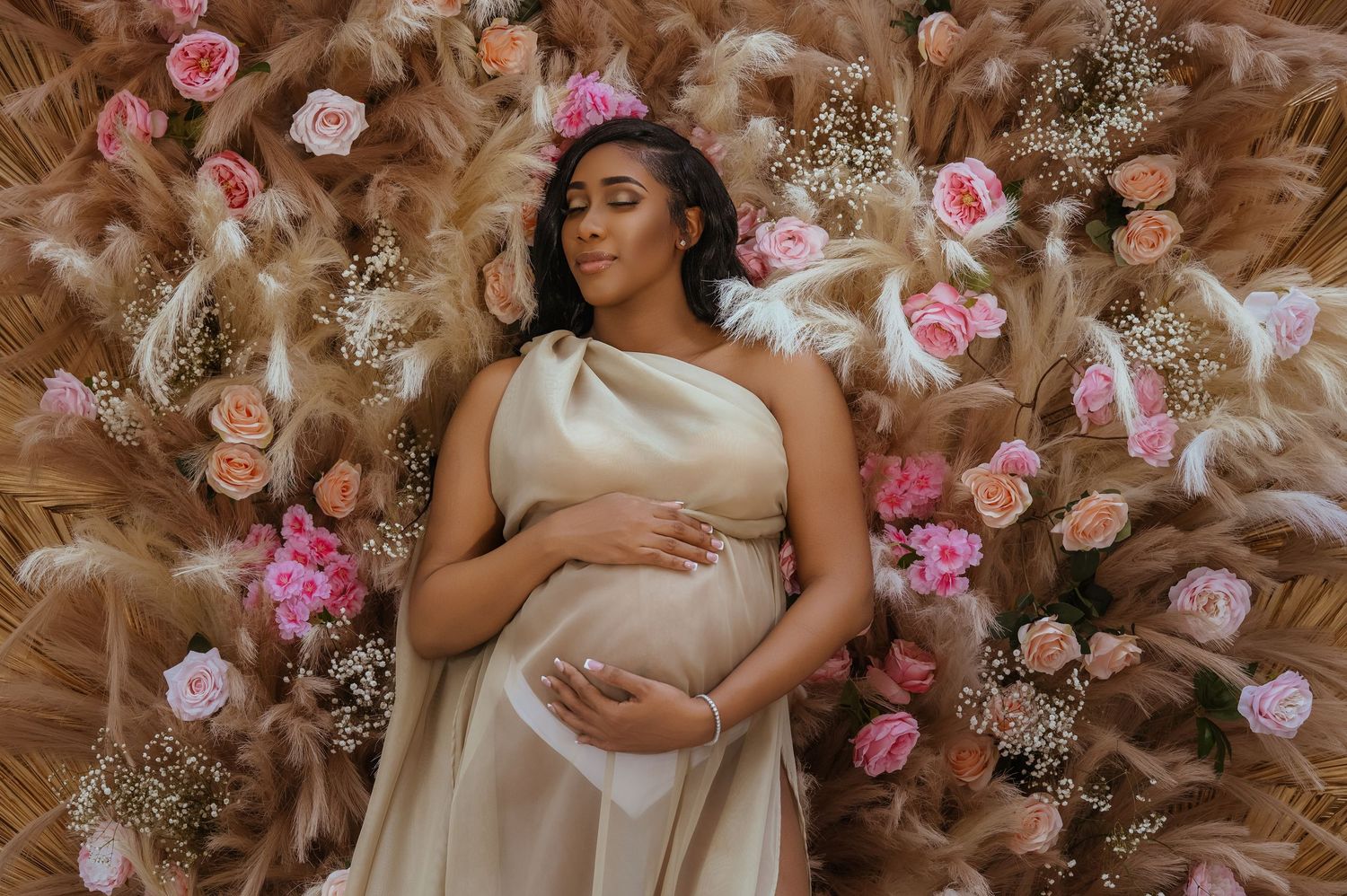 Maternity photo with subject lying on brown pampas grass surrounded by pink roses.