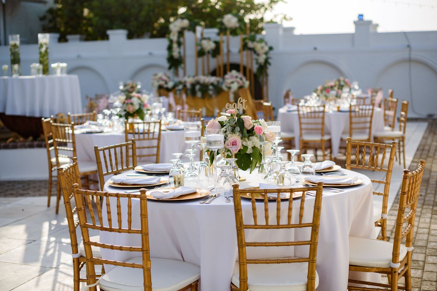 Wedding reception tables set with gold chiavari chairs and white linens in an elegant outdoor setting.