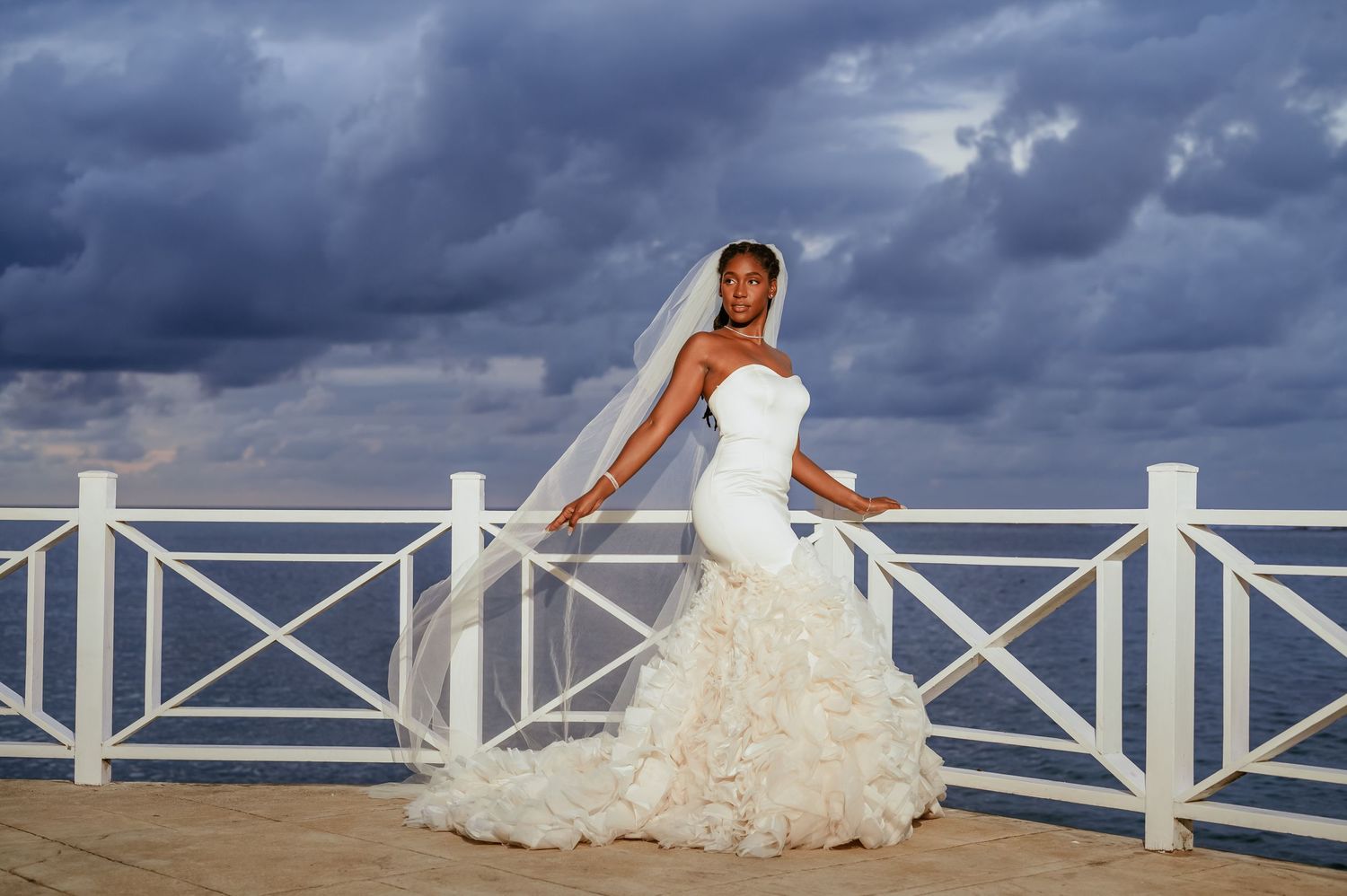 A dramatic bridal portrait against stormy skies and white coastal railings.