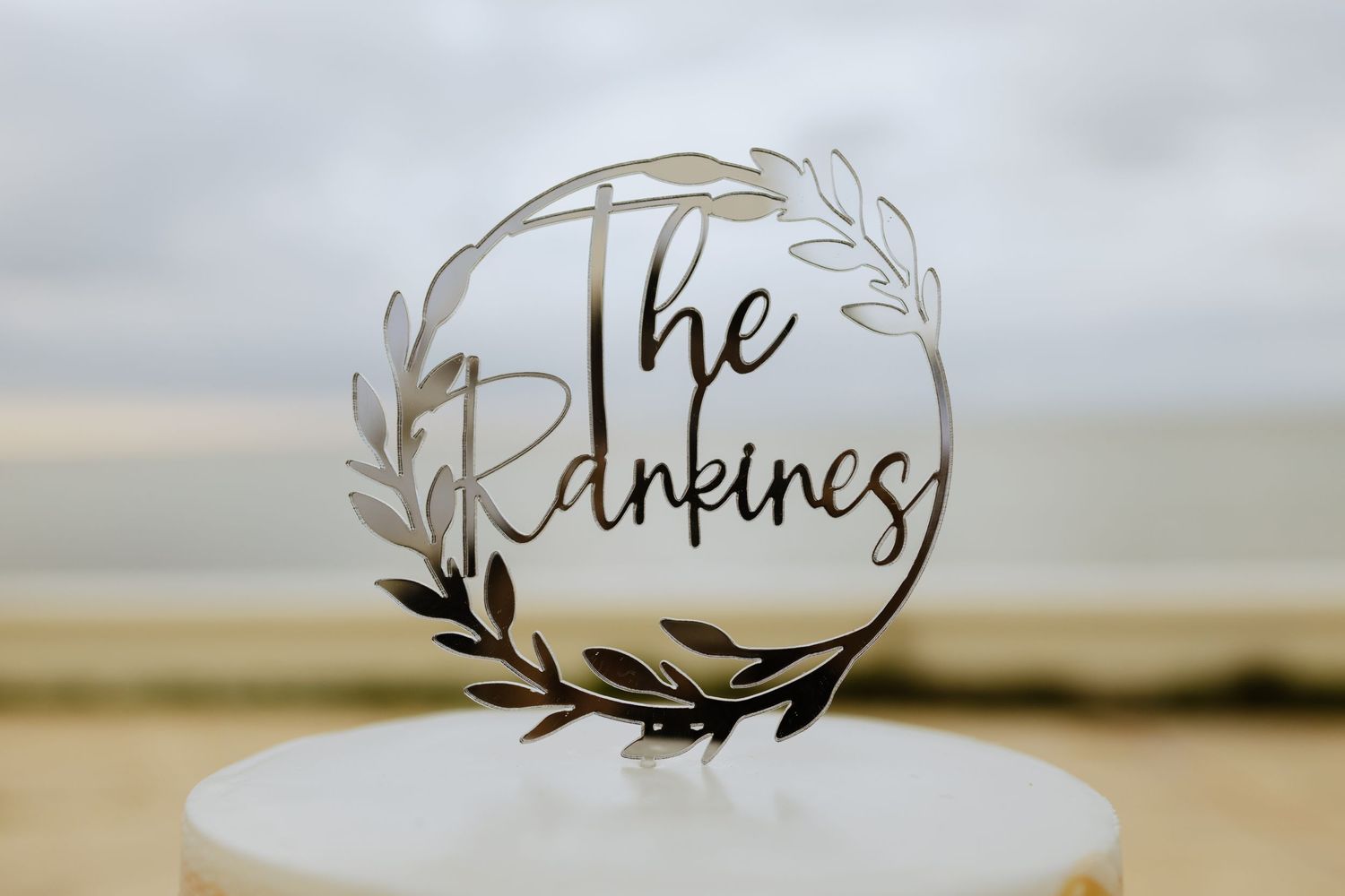 Elegant wedding cake topper with 'The Pinkines' text in a circular floral wreath design.