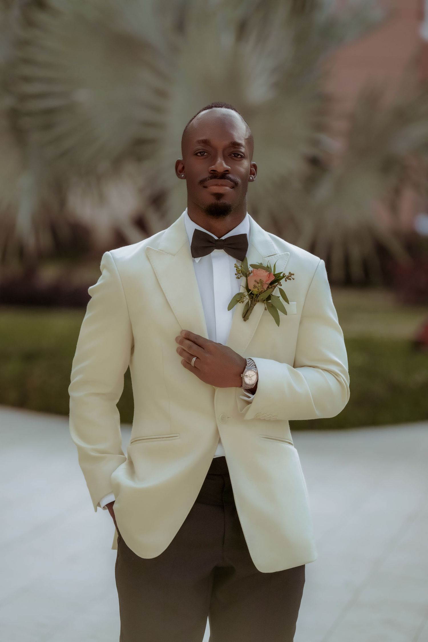 Groom in cream tuxedo jacket and bow tie poses outdoors for wedding portraits.