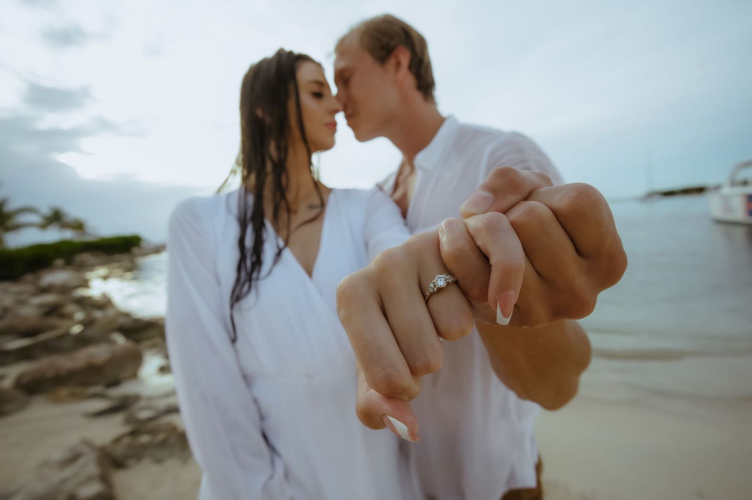 Couple in white outfits sharing tender moments on a beach at dusk.