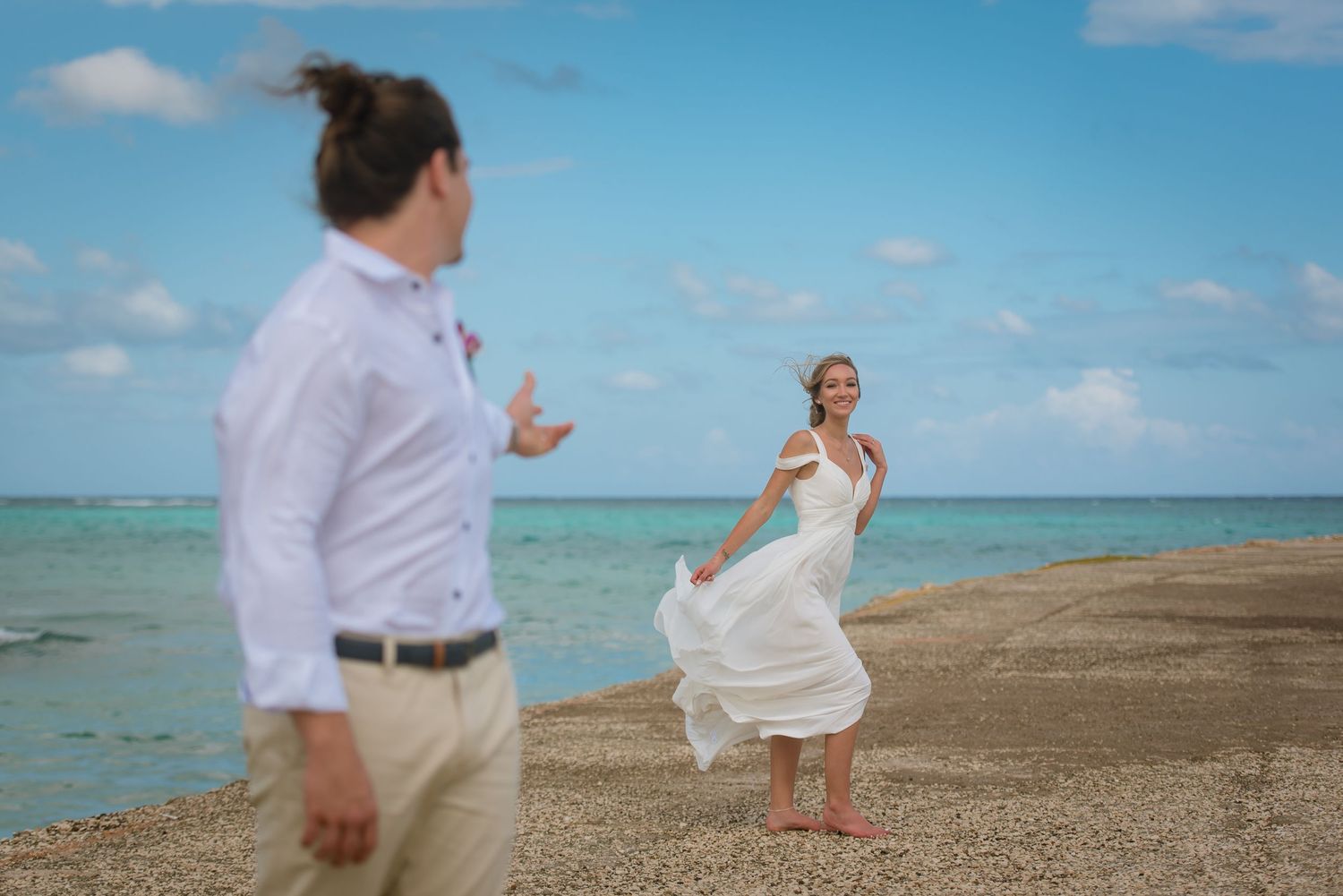 Wedding photoshoot on sandy beach with dramatic blue sky and ocean backdrop.