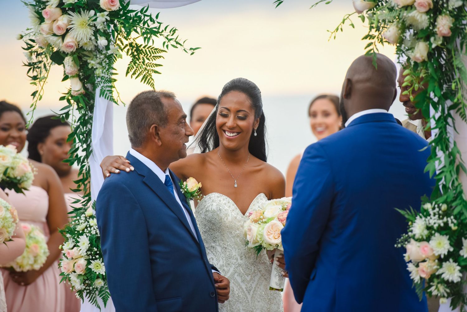 A joyful wedding ceremony takes place under a floral arch with white and peach blooms and greenery.