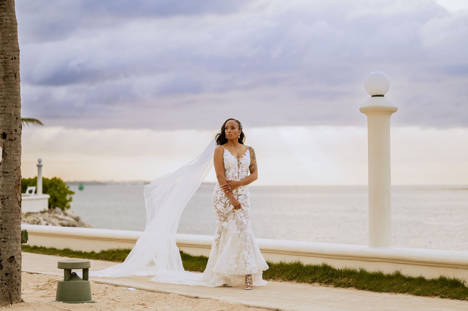 A beachfront wedding scene with palm trees and white architecture in the background.