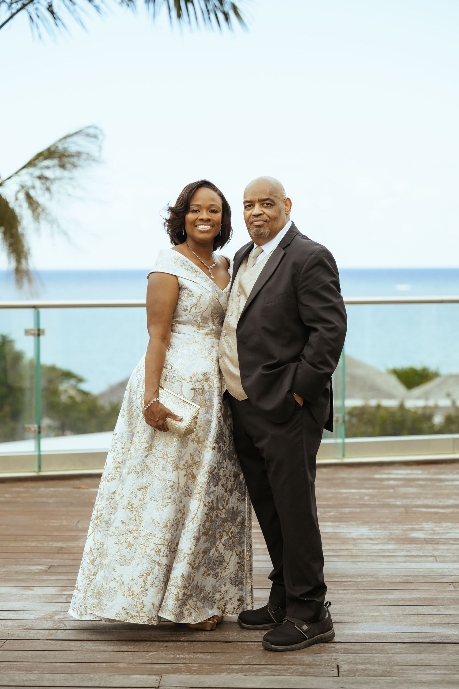 Wedding couple posing on oceanfront deck with palm trees in background.