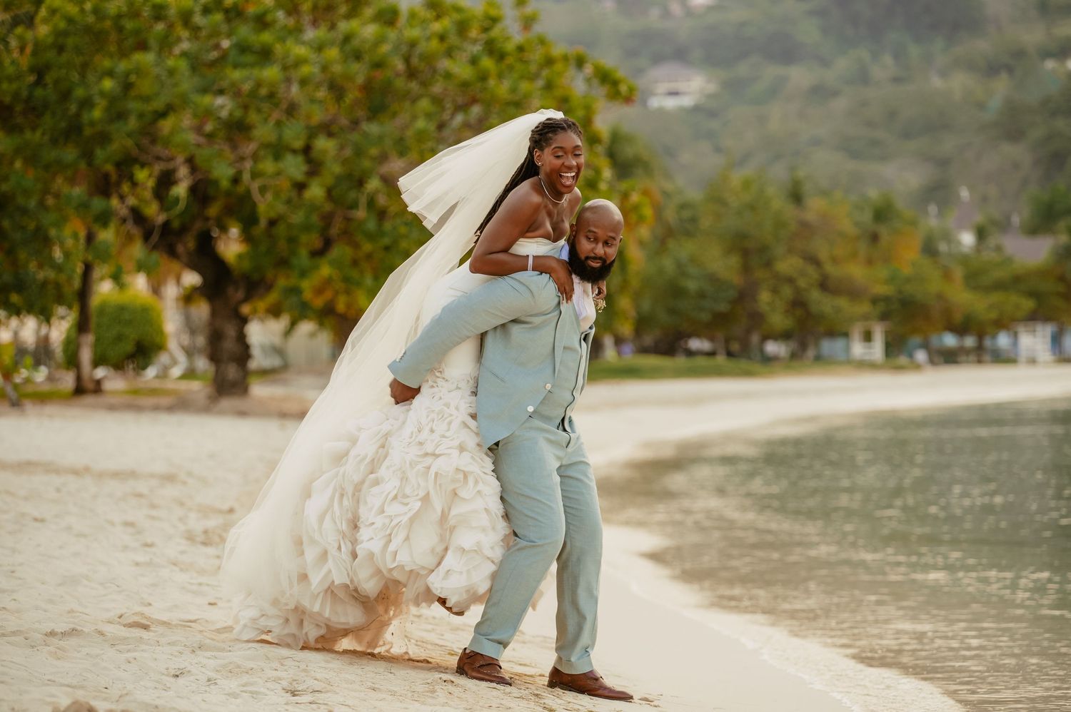 A couple shares a romantic moment on a tropical beach with the bride's veil flowing in the wind.