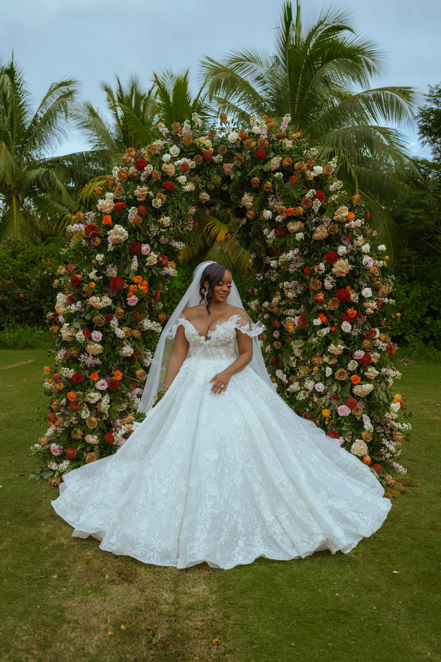 Stunning bridal portrait against a floral arch with coral and white roses in a tropical garden setting.