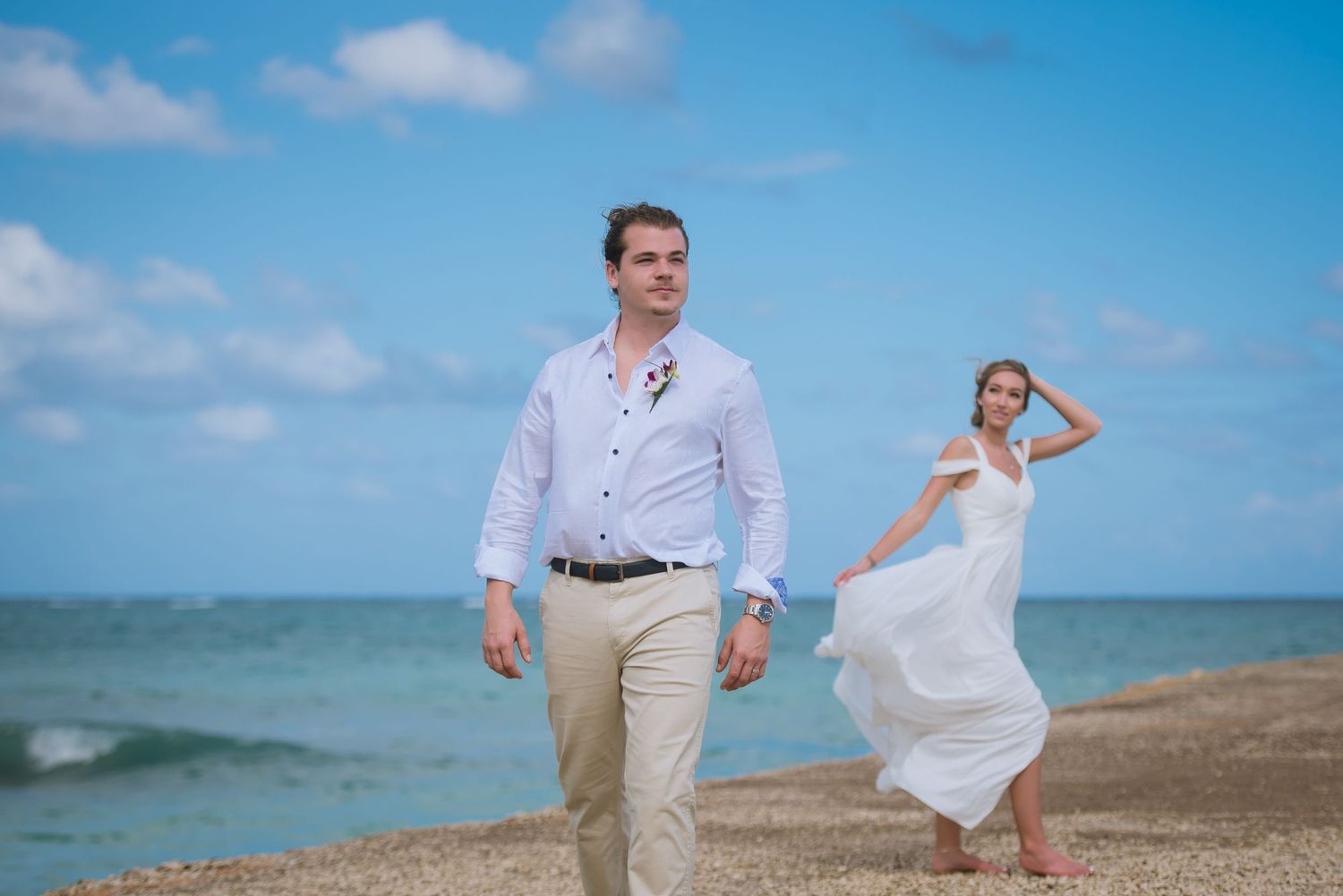 Playful wedding couple posing along shoreline with crystal blue waters in background.