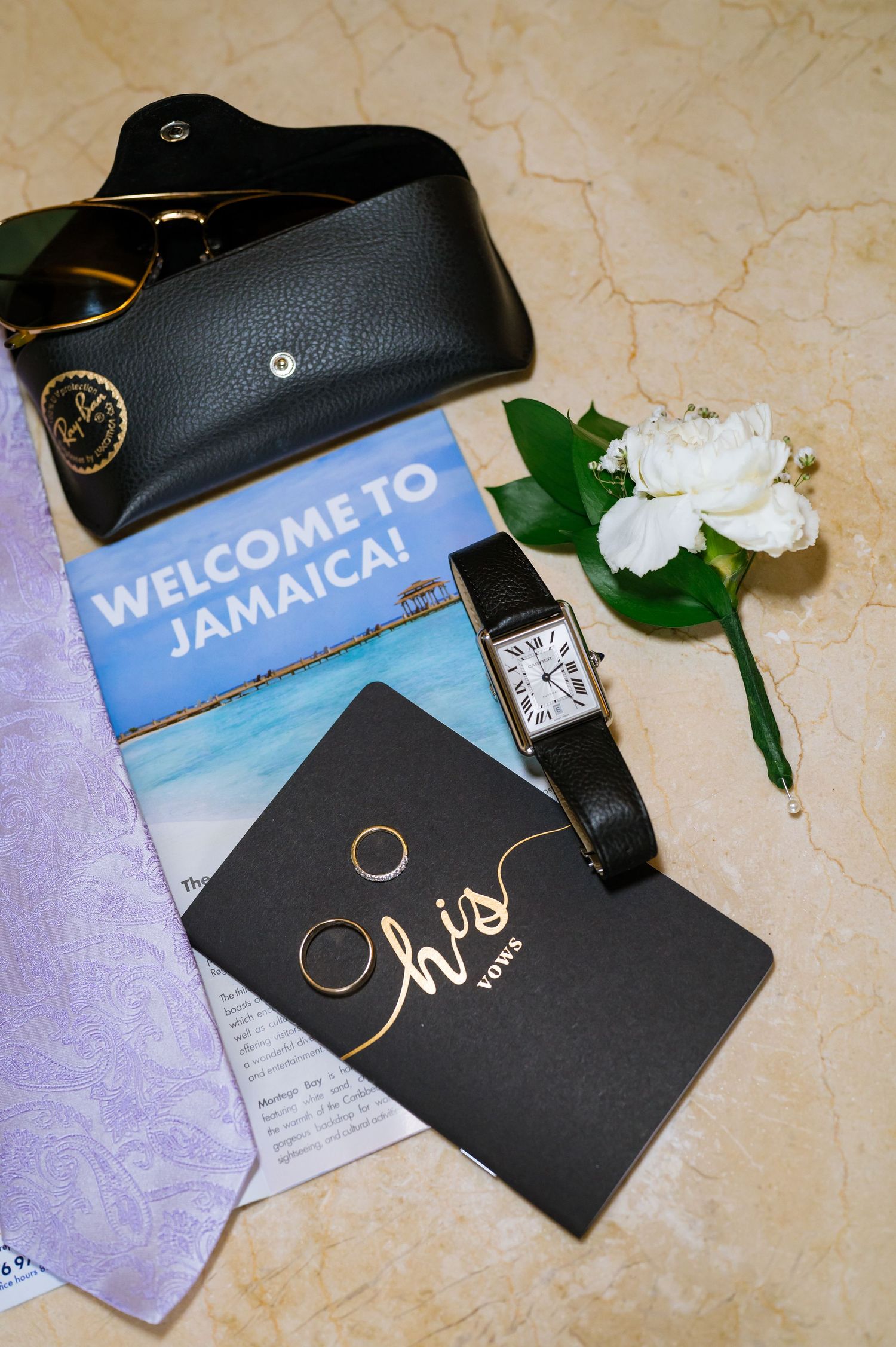 Wedding details flatlay with Jamaica welcome card, rings, watch and white boutonniere.