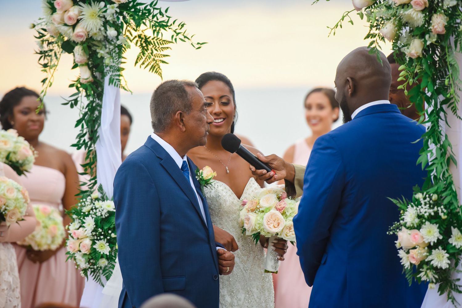 Wedding ceremony under flower-adorned arch with white and blush floral arrangements.
