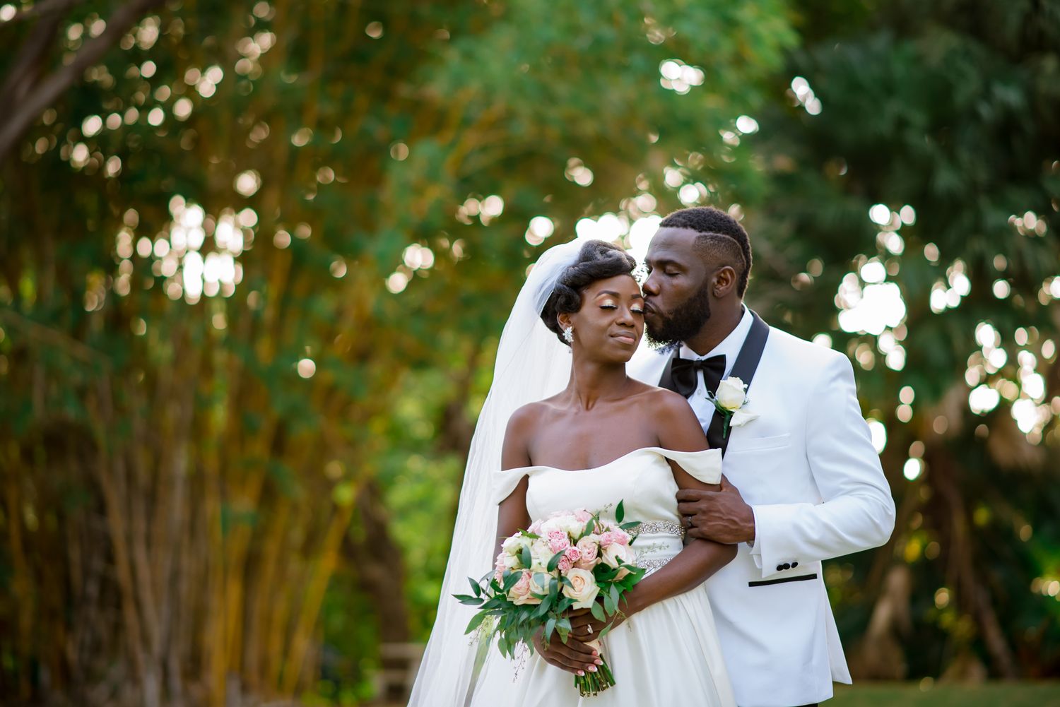 Romantic wedding couple embraces in a garden setting with soft bokeh lighting.
