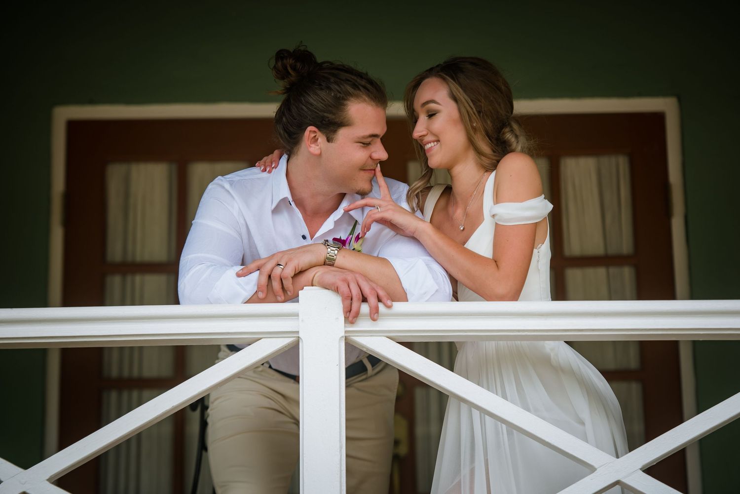 Couple sharing intimate moments along a white railing on a porch.