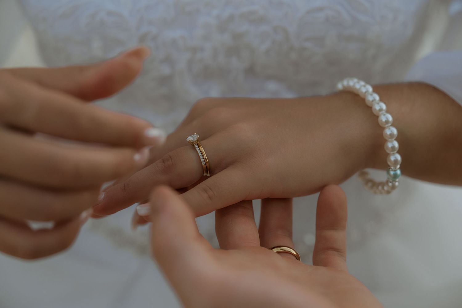 Close-up of hands with pearl bracelet and wedding rings during a ceremony.